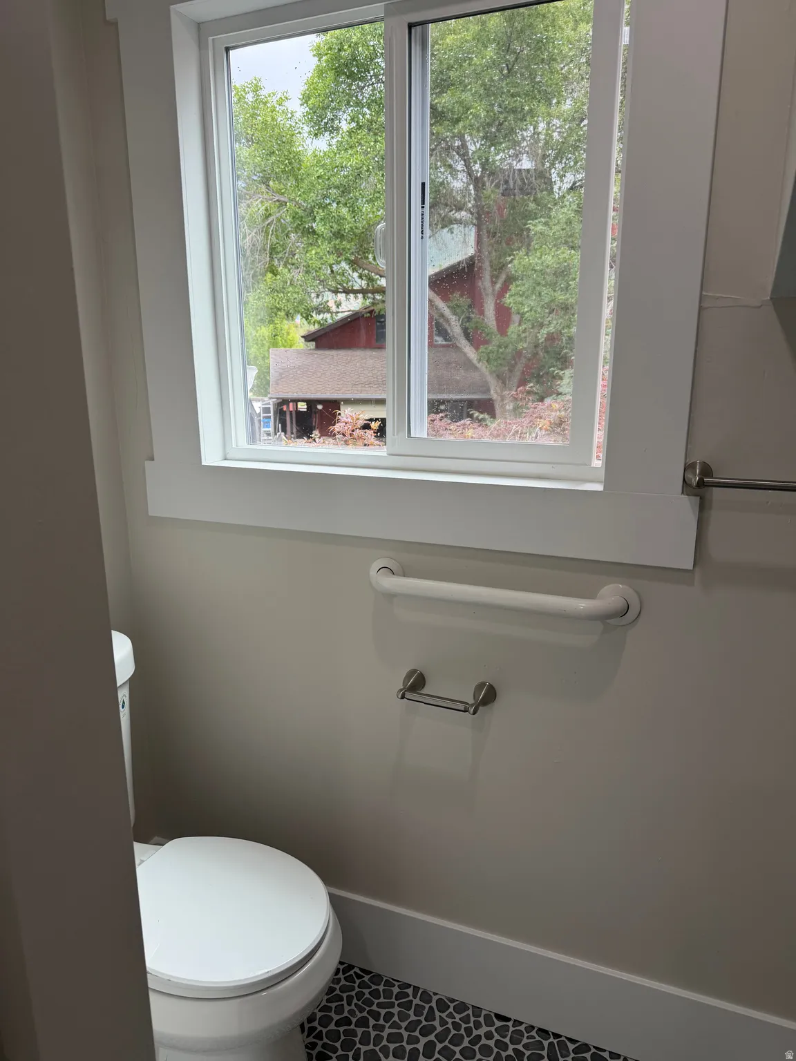 Bathroom featuring a white toilet, pebble-style flooring, a sliding window with white trim, a towel bar, and a grab bar