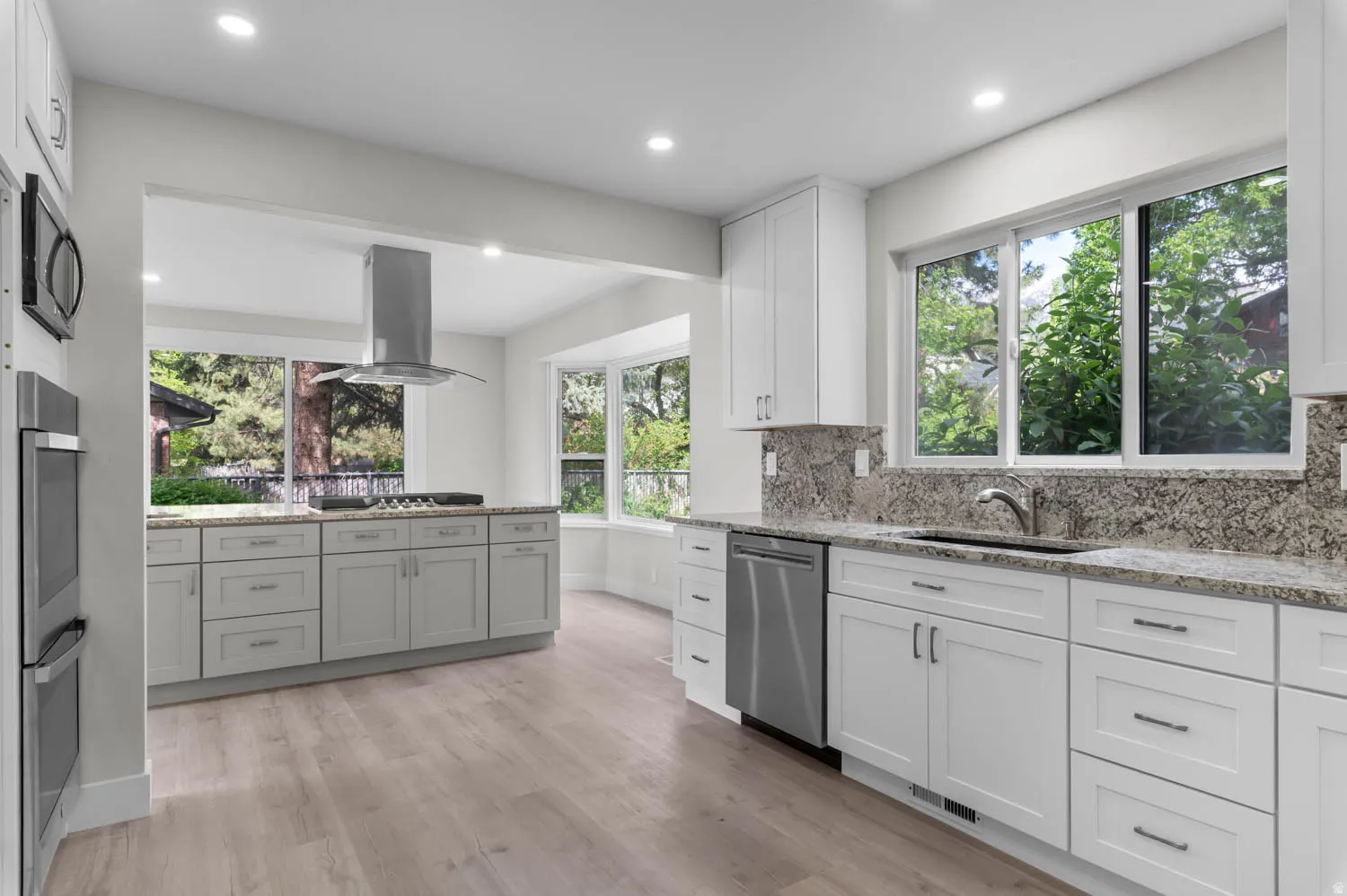 Kitchen with light stone countertops, white cabinets, island range hood, tasteful backsplash, and recessed lighting