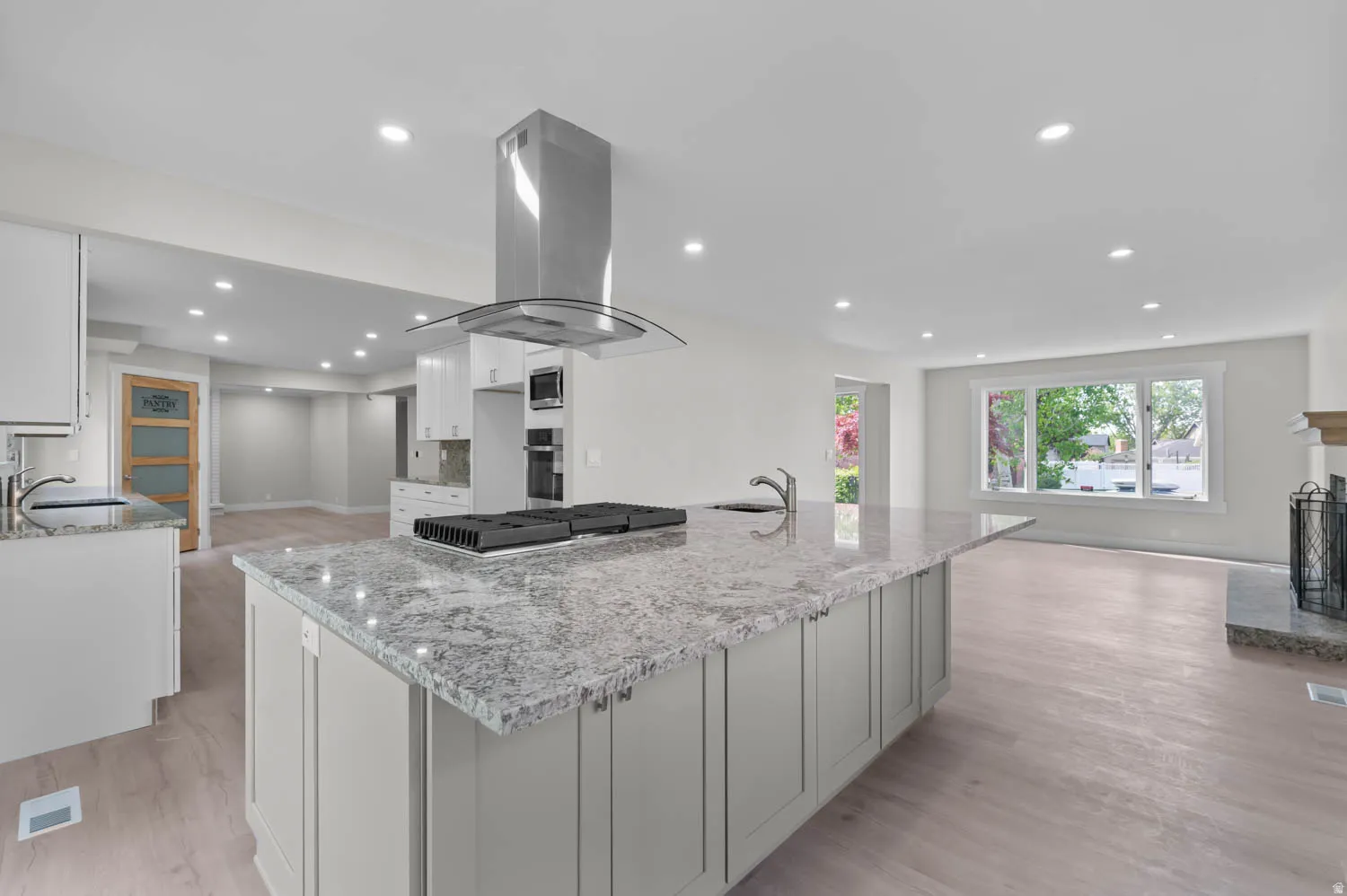 Kitchen with light stone counters, island exhaust hood, recessed lighting, open floor plan, and light wood finished floors