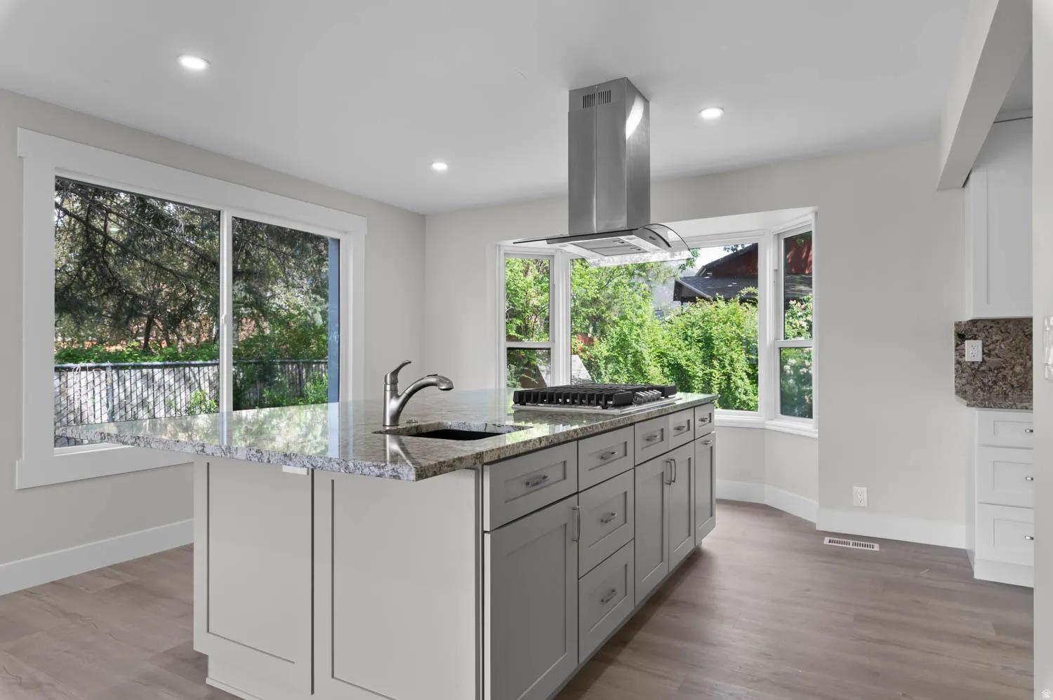 Kitchen featuring light stone counters, island exhaust hood, light wood finished floors, a kitchen island with sink, and stainless steel gas stovetop