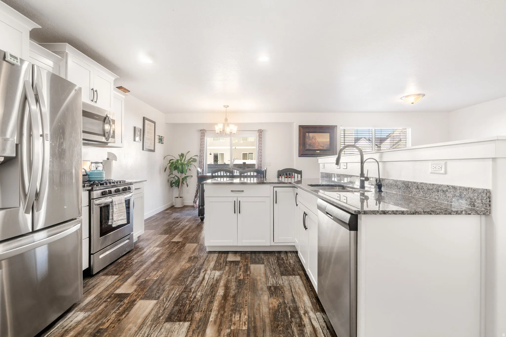 Kitchen featuring a peninsula, stainless steel appliances, white cabinetry, dark wood-type flooring, and dark stone counters