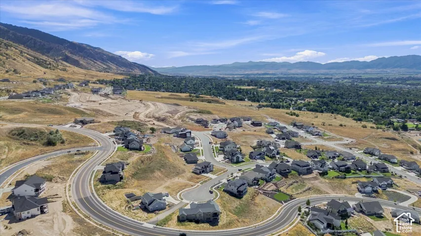 Curved asphalt roadways winding through a developing residential community, surrounded by arid hillsides and distant green valleys
