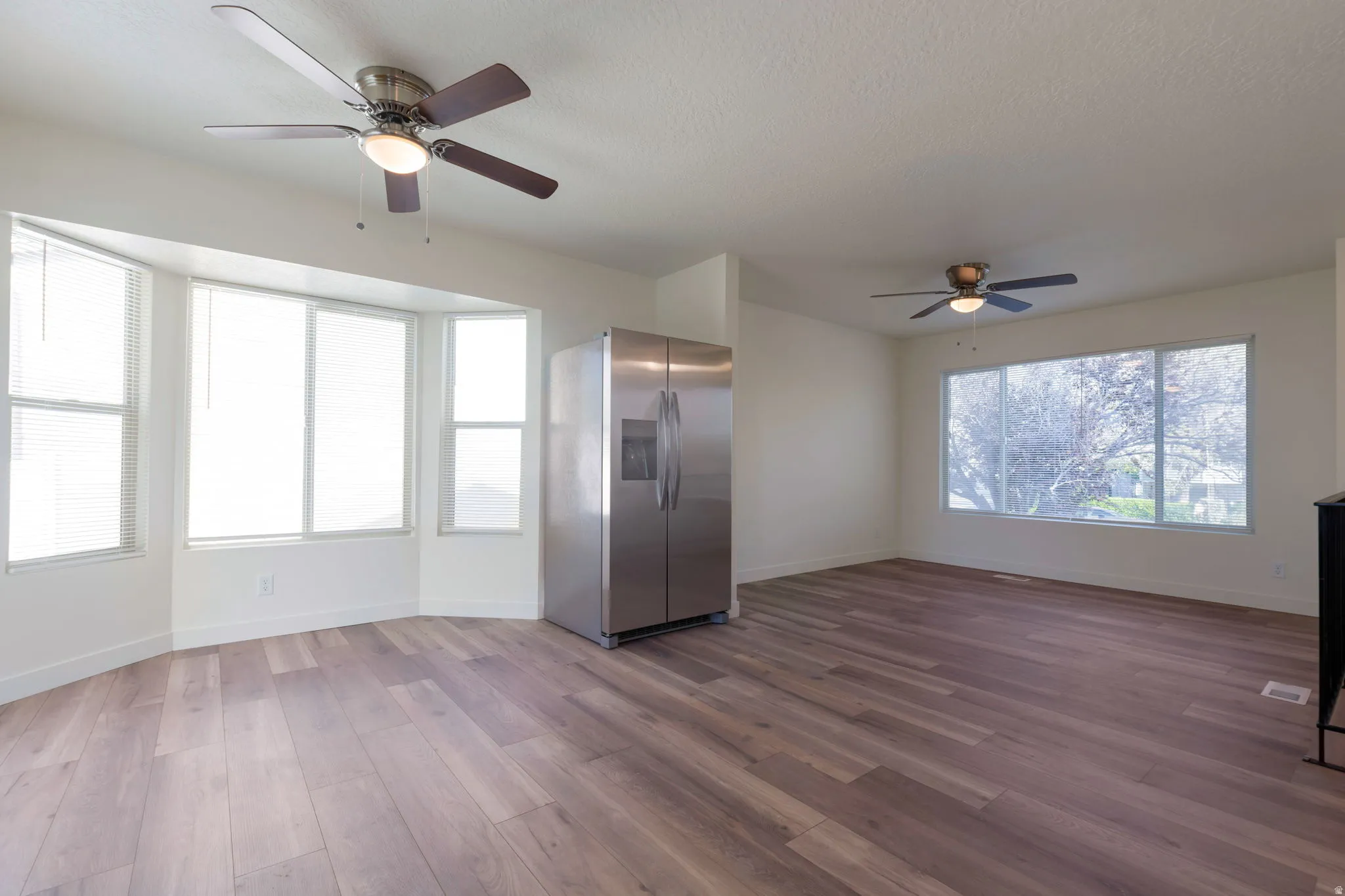 Unfurnished living room featuring ceiling fan, dark wood-style floors, and a textured ceiling