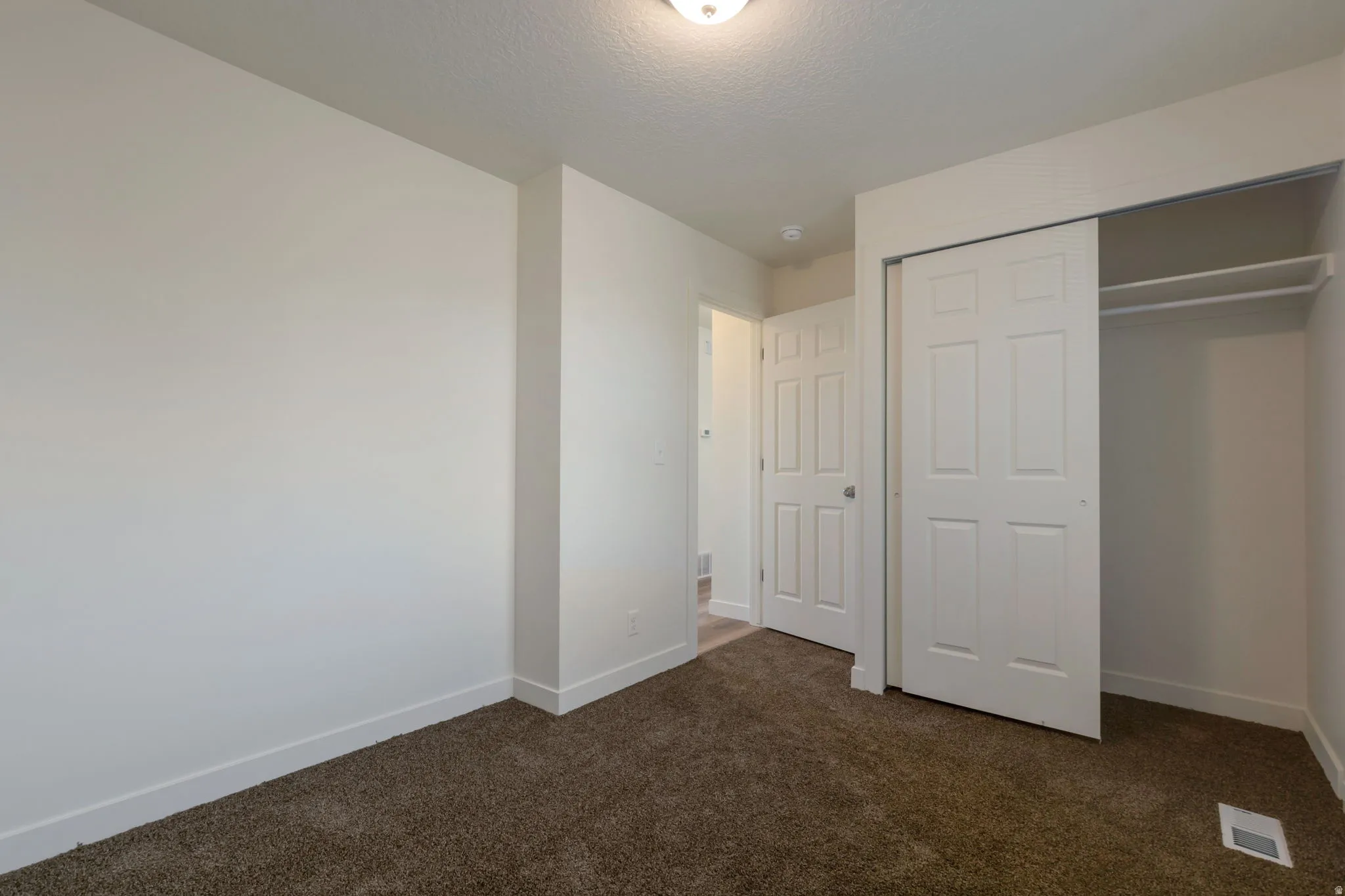Unfurnished bedroom featuring dark colored carpet, a closet, and a textured ceiling