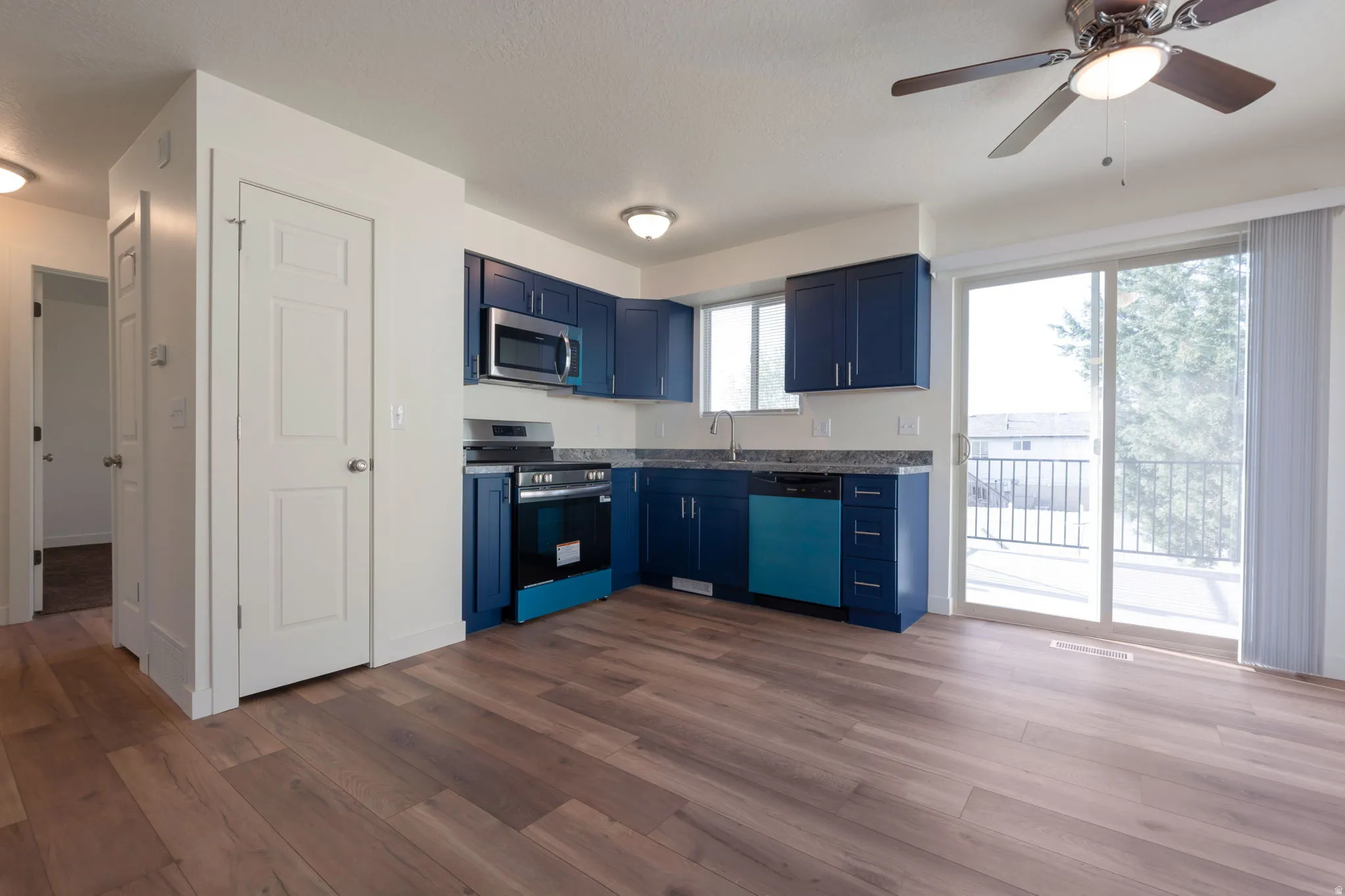 Kitchen featuring stainless steel appliances, dark wood-type flooring, blue cabinetry, ceiling fan, and dark countertops