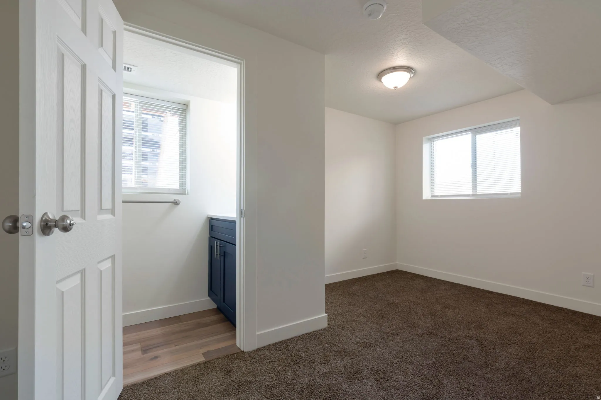 Unfurnished bedroom featuring multiple windows, dark colored carpet, connected bathroom, and a textured ceiling