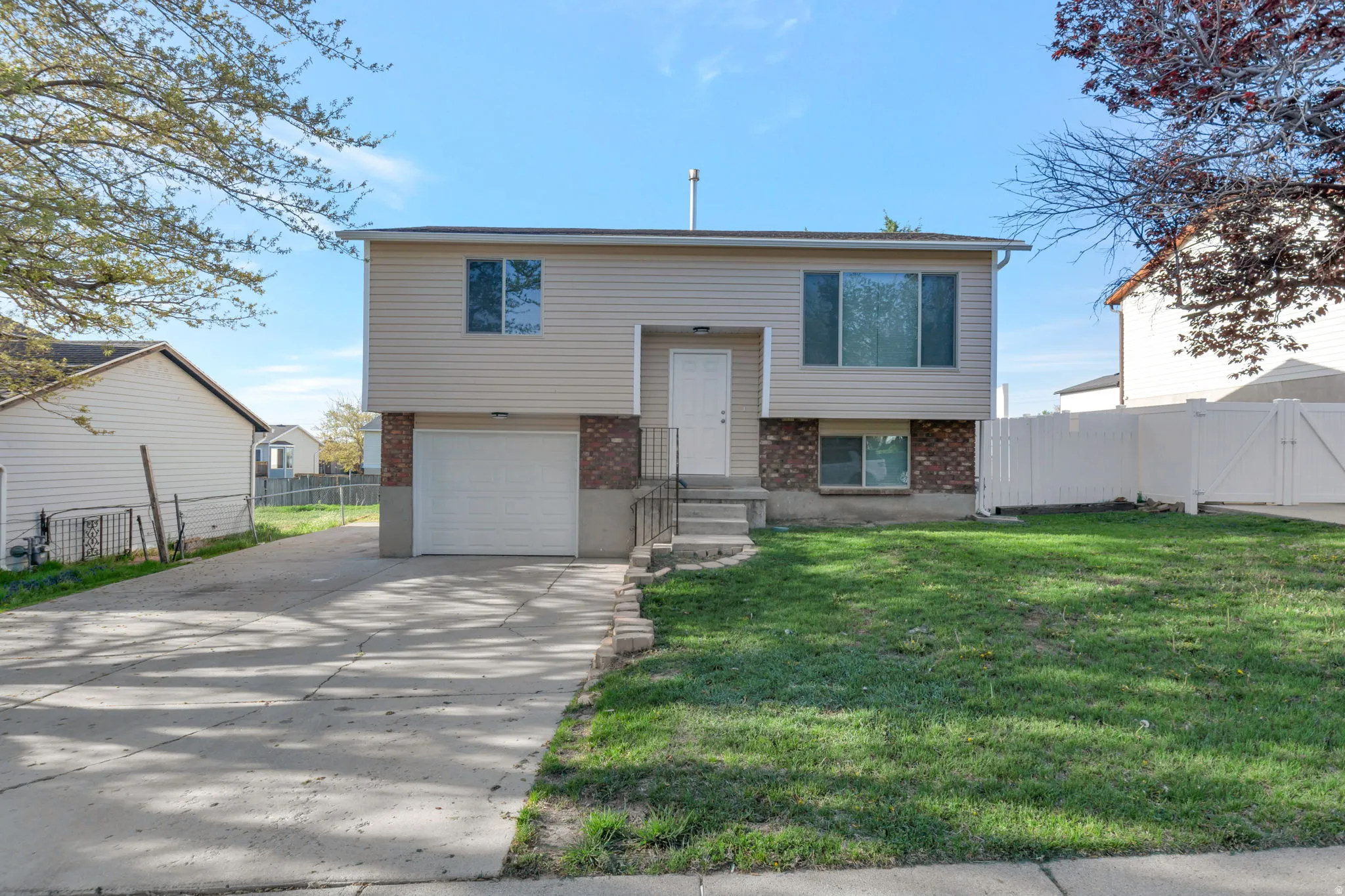 Split foyer home featuring brick siding, a garage, driveway, and a gate