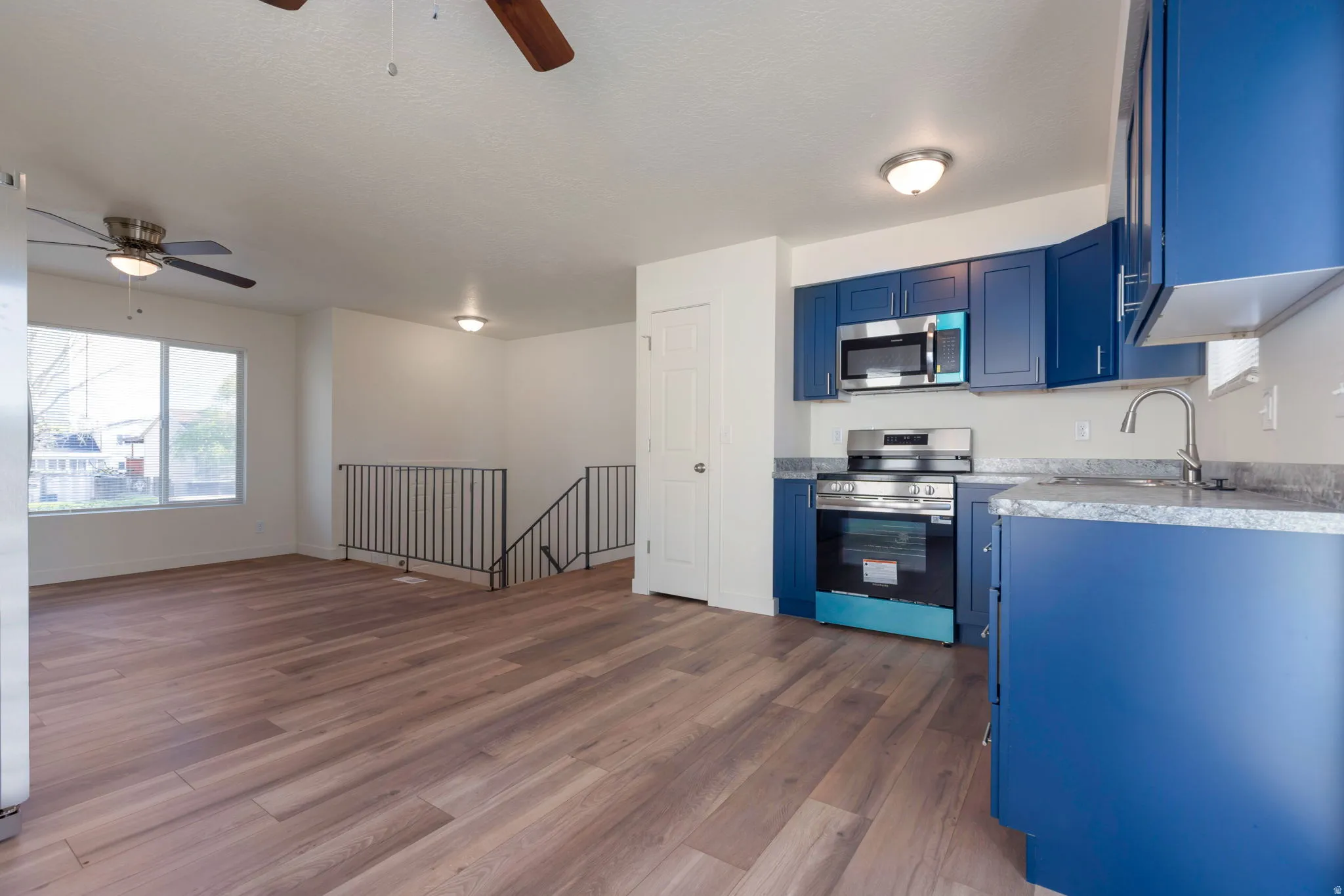 Kitchen featuring stainless steel appliances, a ceiling fan, blue cabinetry, and dark wood finished floors
