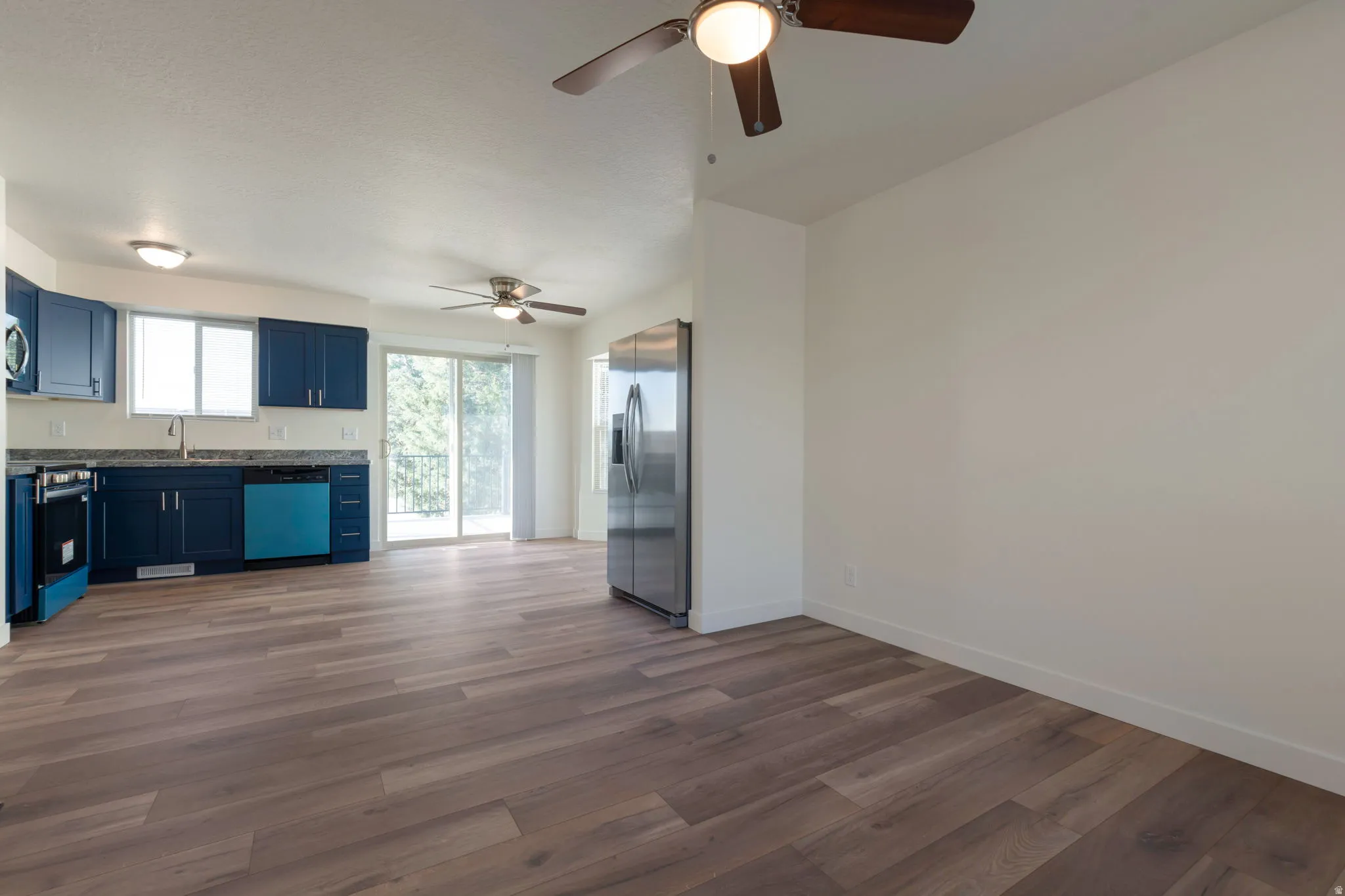 Kitchen with stainless steel appliances, blue cabinets, dark wood-style floors, and a ceiling fan