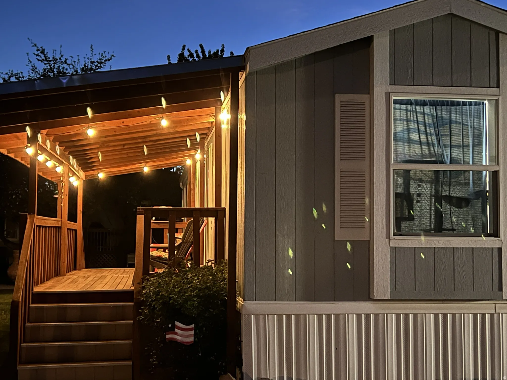 Covered porch with wood decking and railing, featuring string lighting