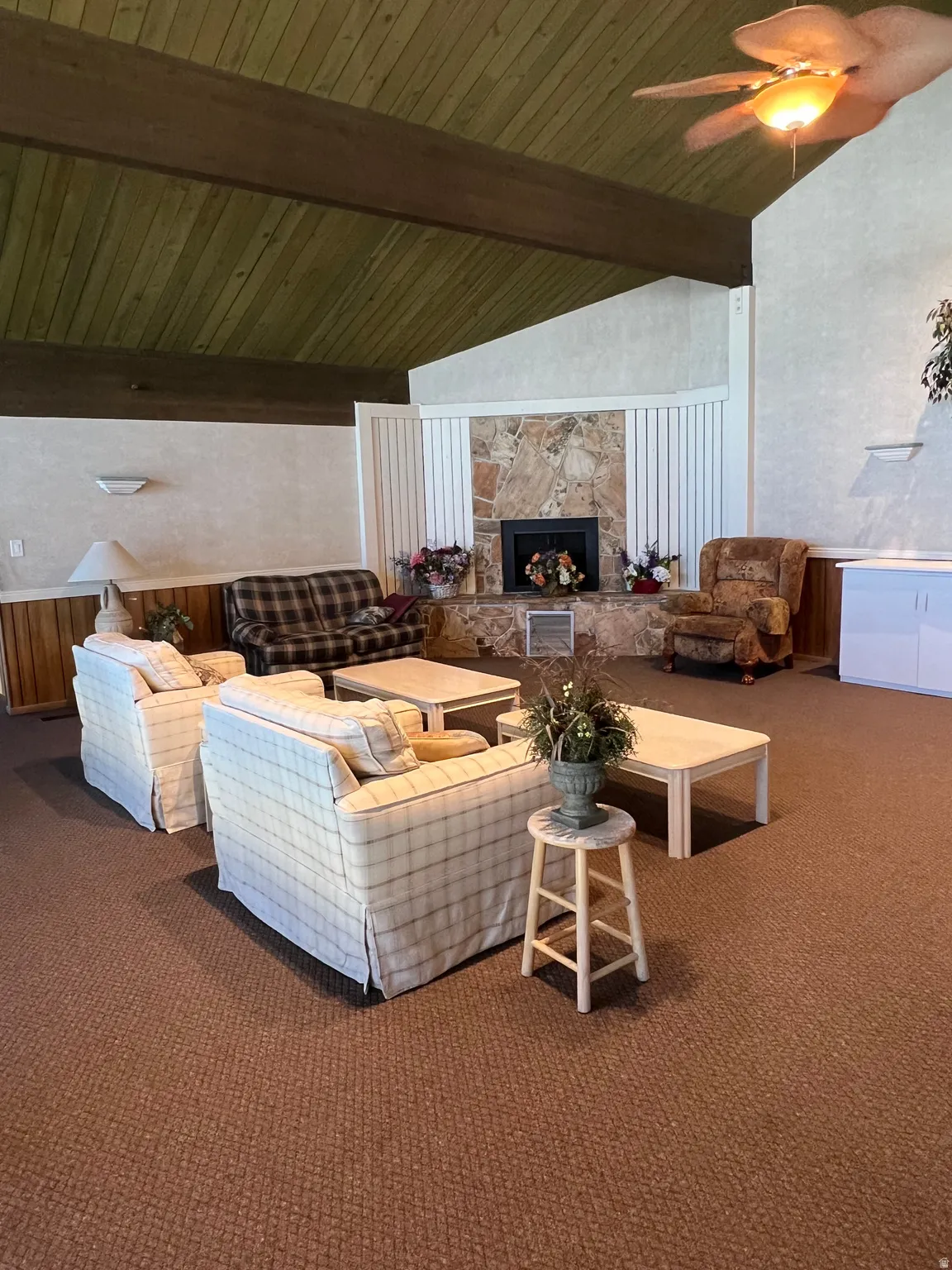 Spacious common area featuring a stone-clad fireplace, textured walls, and a vaulted ceiling with exposed wood beams