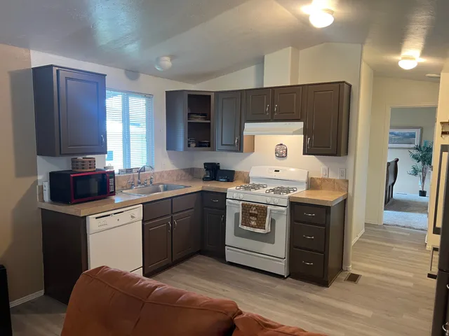 Kitchen featuring white appliances, light LVT floors, light countertops, vaulted ceiling, and open shelves