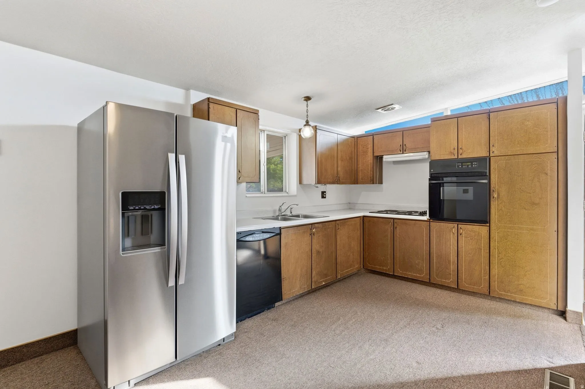 Kitchen with black appliances, light countertops, wood finish cabinetry, and decorative light fixtures
