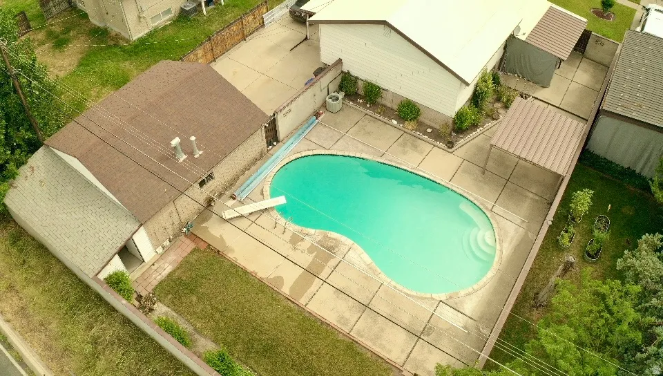 Kidney-shaped swimming pool with concrete decking, a diving board, and integrated steps
