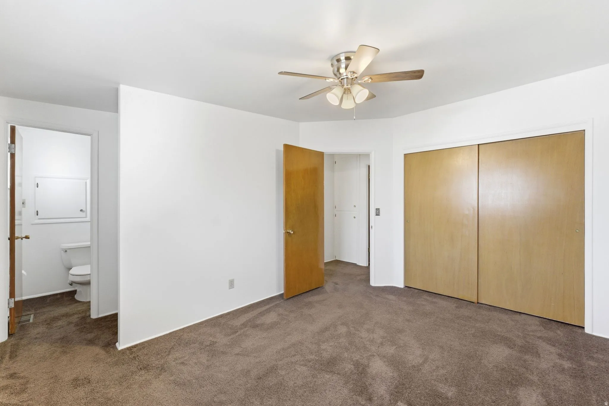 Unfurnished bedroom featuring dark carpet, ensuite bath, a closet, and a ceiling fan