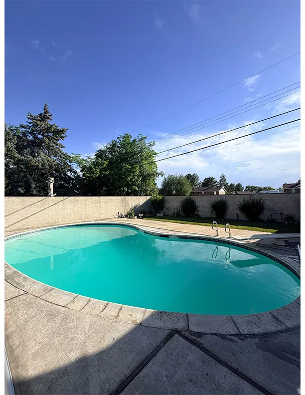 Freeform swimming pool with concrete coping and perimeter paving, surrounded by a concrete block privacy wall