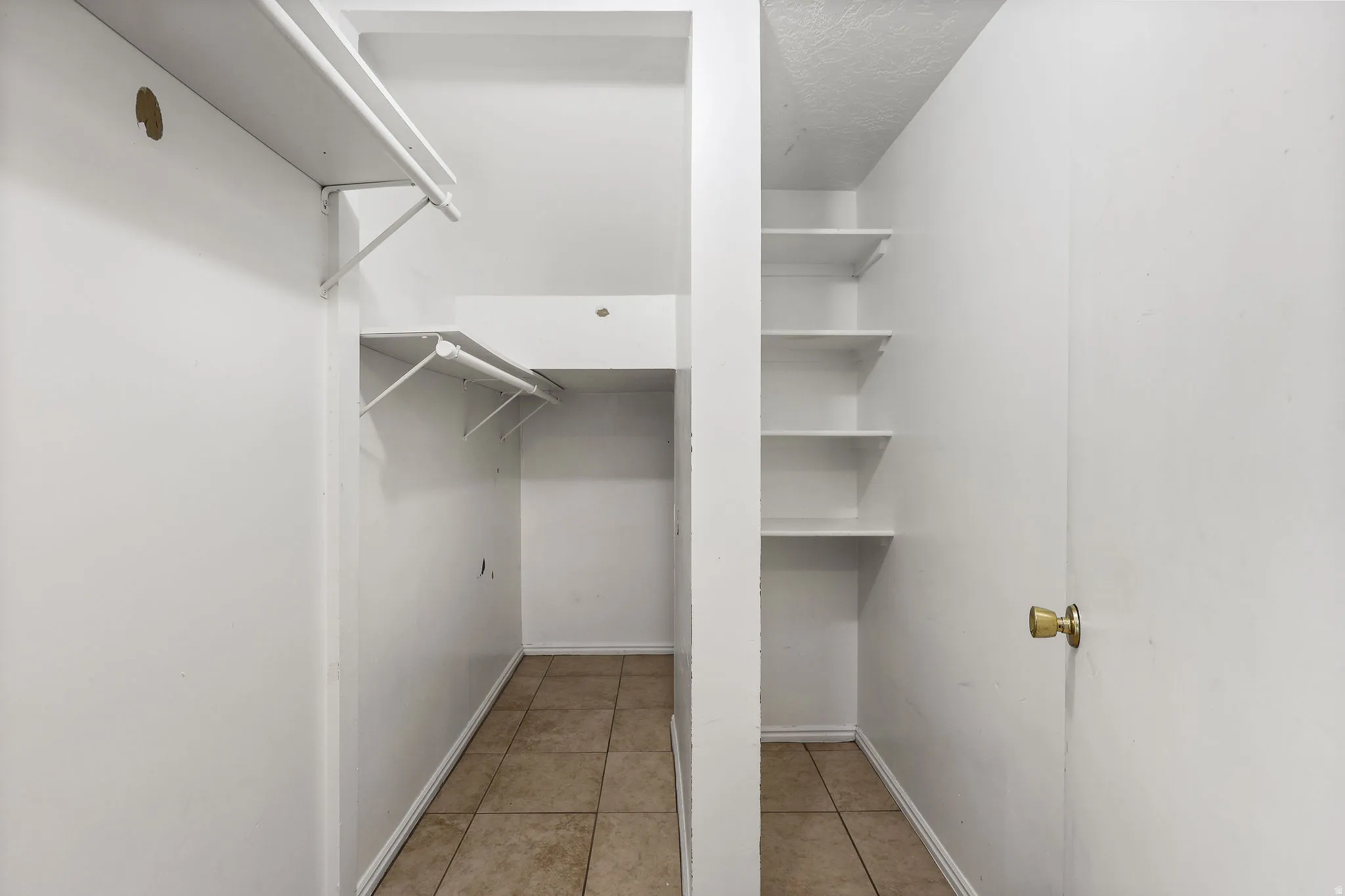 Functional closet space featuring tile flooring, multiple hanging rods, and integrated shelving