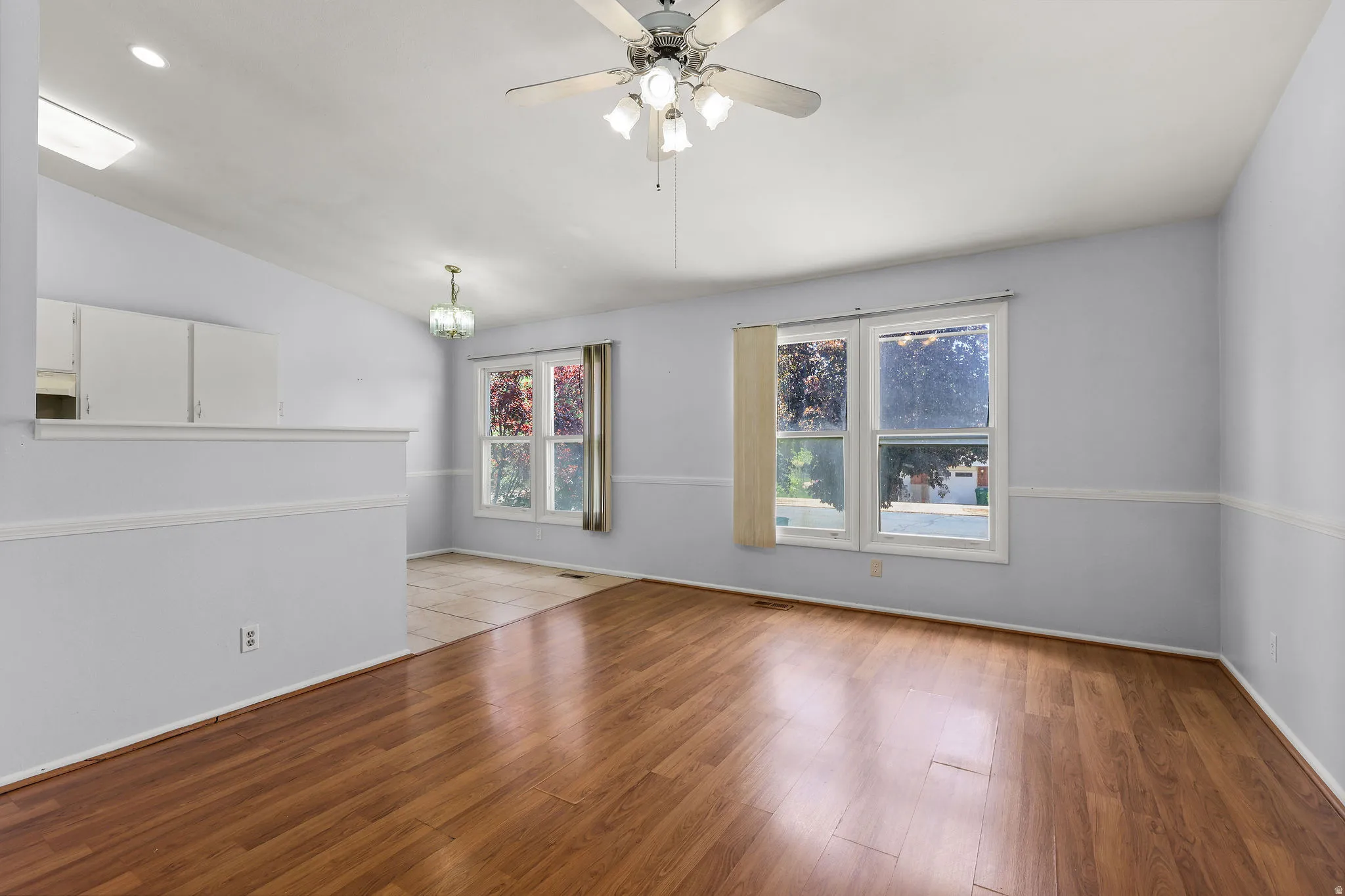 Spacious room featuring wood-finish flooring, light grey walls, and a ceiling fan with integrated lighting