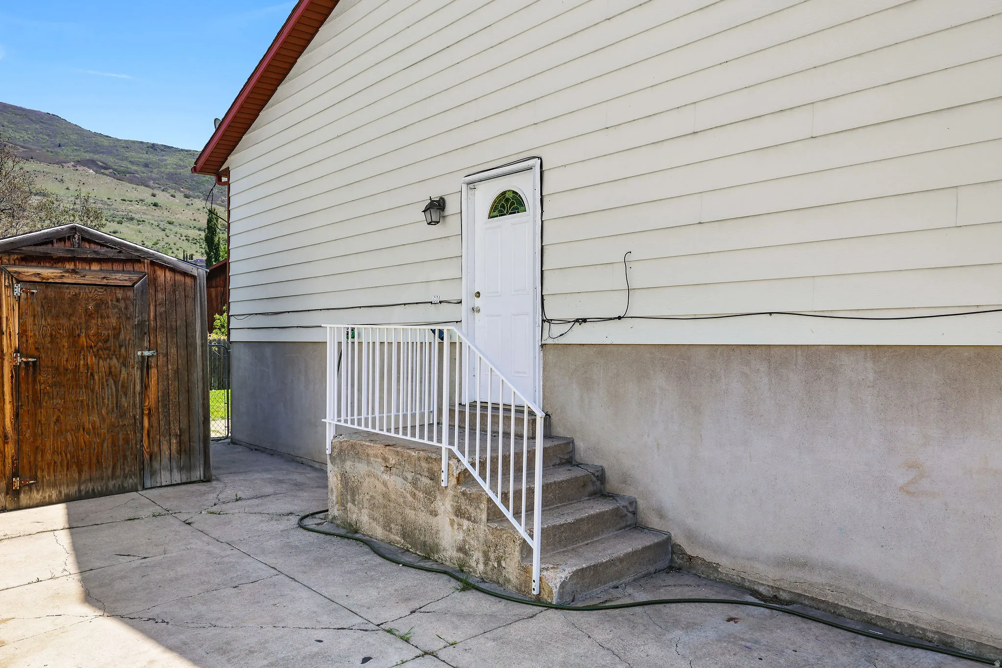 Exterior side entrance featuring concrete steps with white metal railings, a white door with an arched window, and an exterior wall light fixture