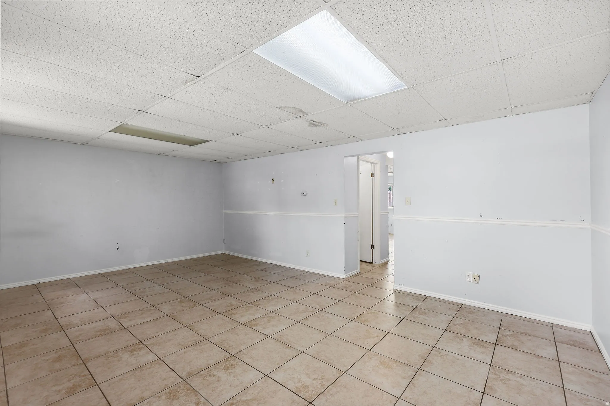 Spacious room featuring neutral paint, tile flooring, drop ceiling with recessed lighting, and a doorway