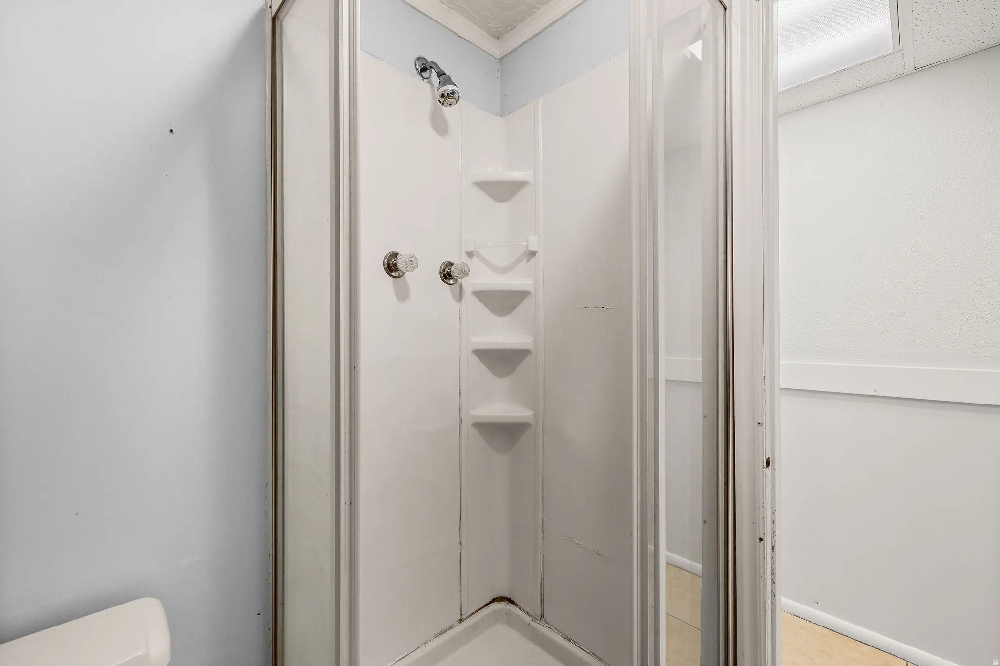 Enclosed shower with clear glass door, chrome fixtures, and built-in shelving