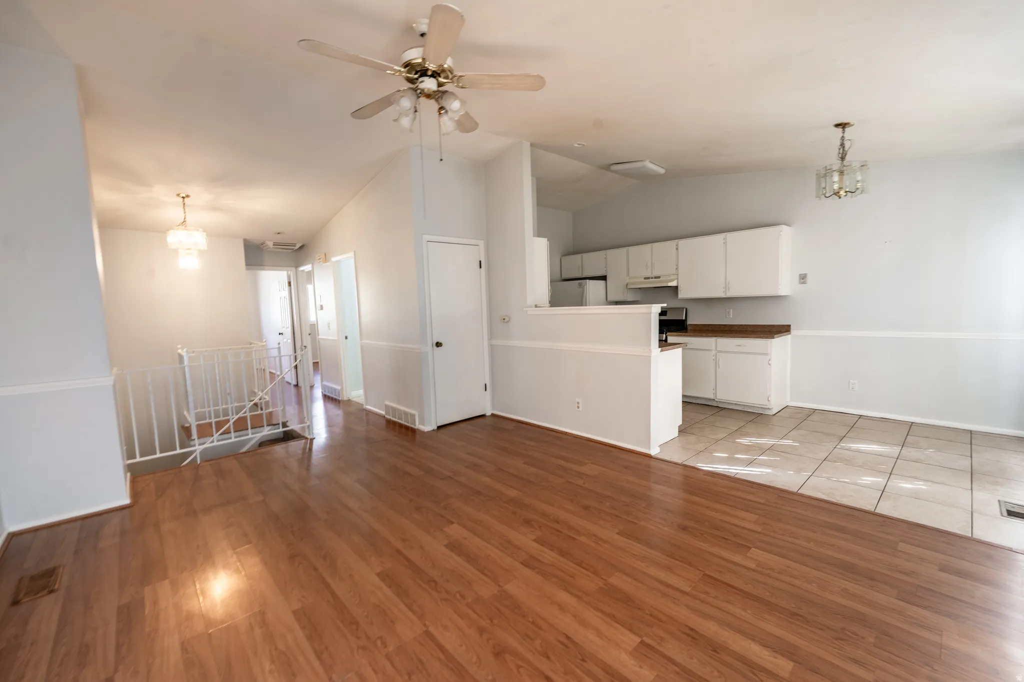 Unfurnished living room with suspended lighting, vaulted ceiling, a ceiling fan, and light wood-style flooring