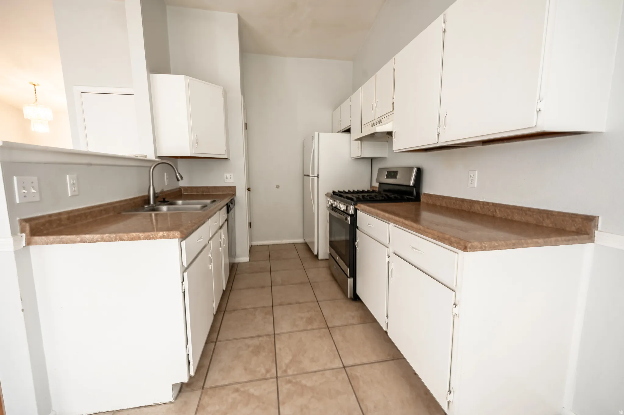 Kitchen featuring stainless steel appliances, dark countertops, white cabinetry, and light tile patterned floors