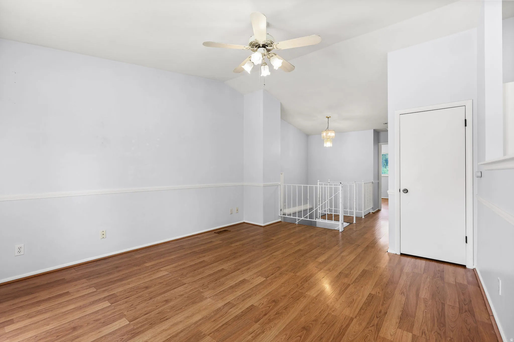 Spacious room featuring wood-finish flooring, light blue walls with white chair rail molding, and a ceiling fan with integrated lighting
