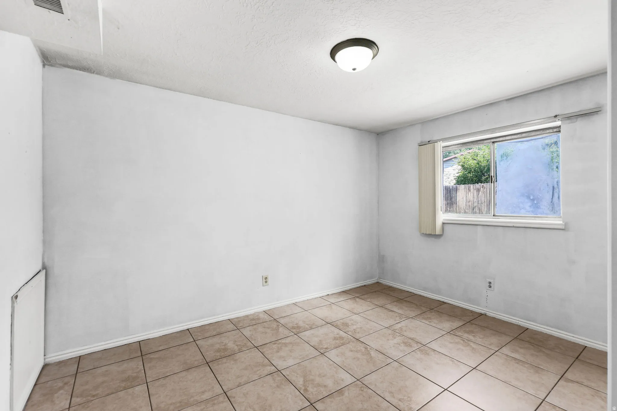 Room featuring square tile flooring, white baseboards, and a single window with a privacy screen