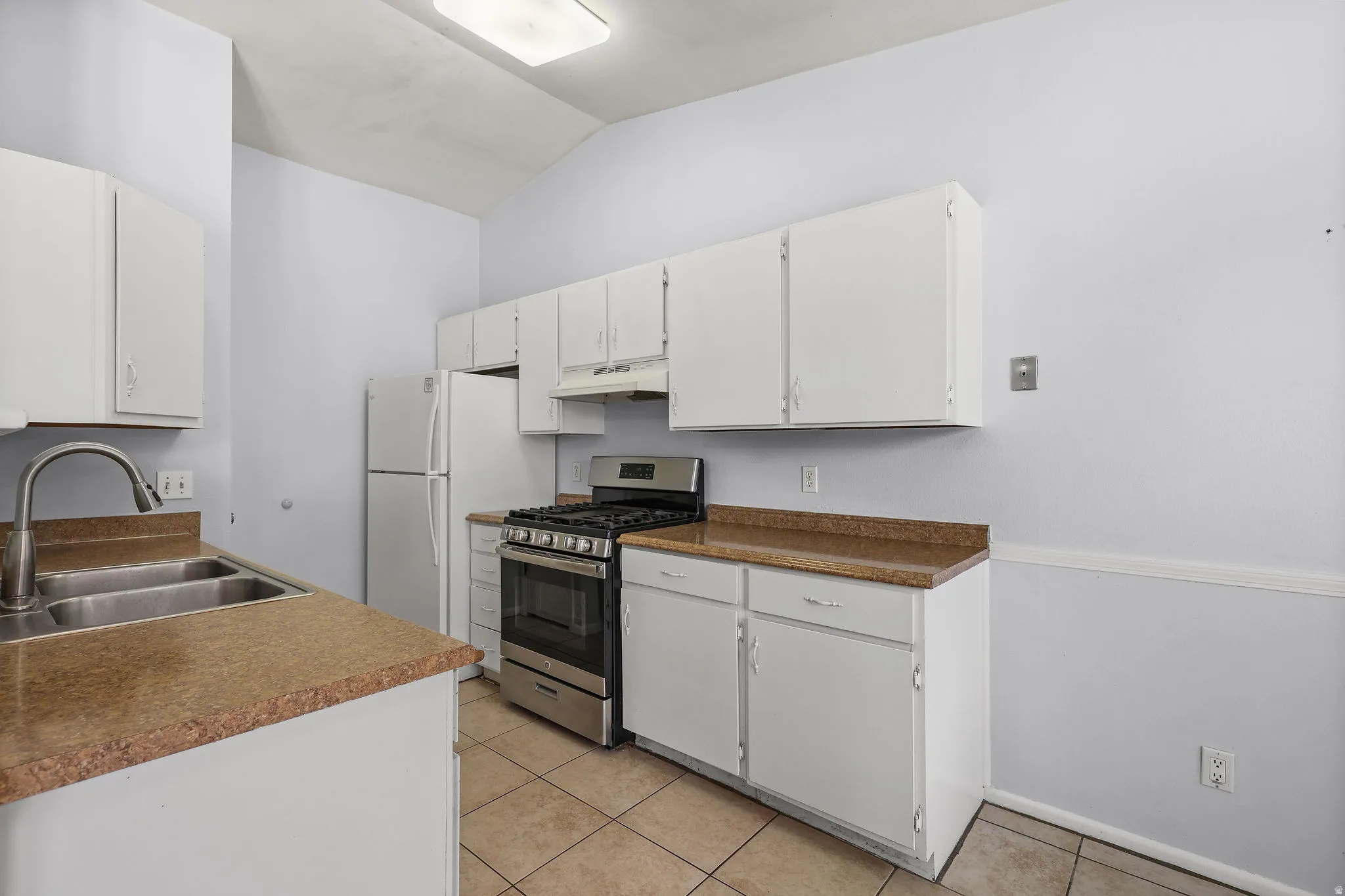 Kitchen featuring white cabinetry, light-toned countertops, a stainless steel range with overhead hood, a double basin sink with a brushed metal faucet, and tile flooring