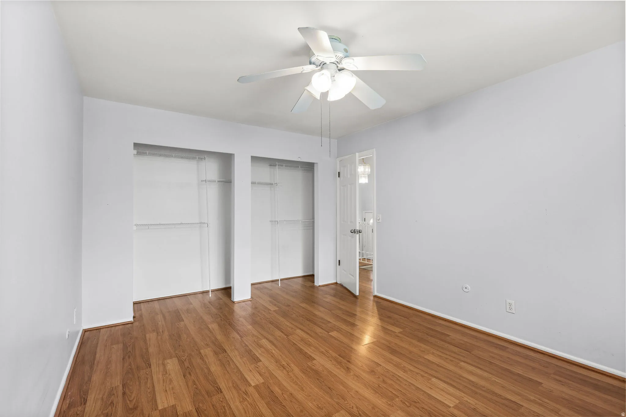 Room featuring wood-finish flooring, two open closet spaces with shelving, a ceiling fan with integrated lighting, and light gray wall paint