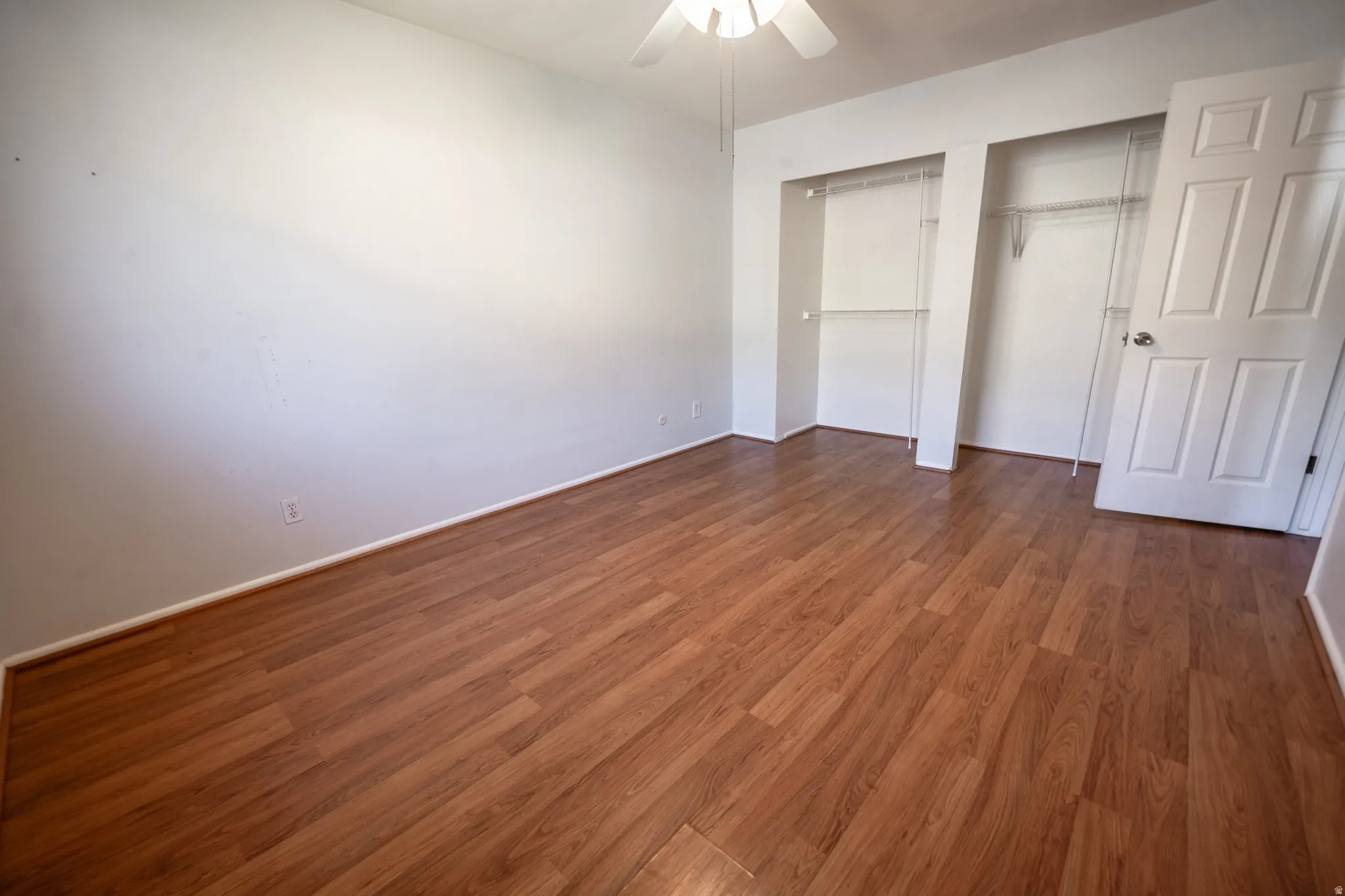 Unfurnished bedroom featuring dark wood finished floors, a ceiling fan, and two closets