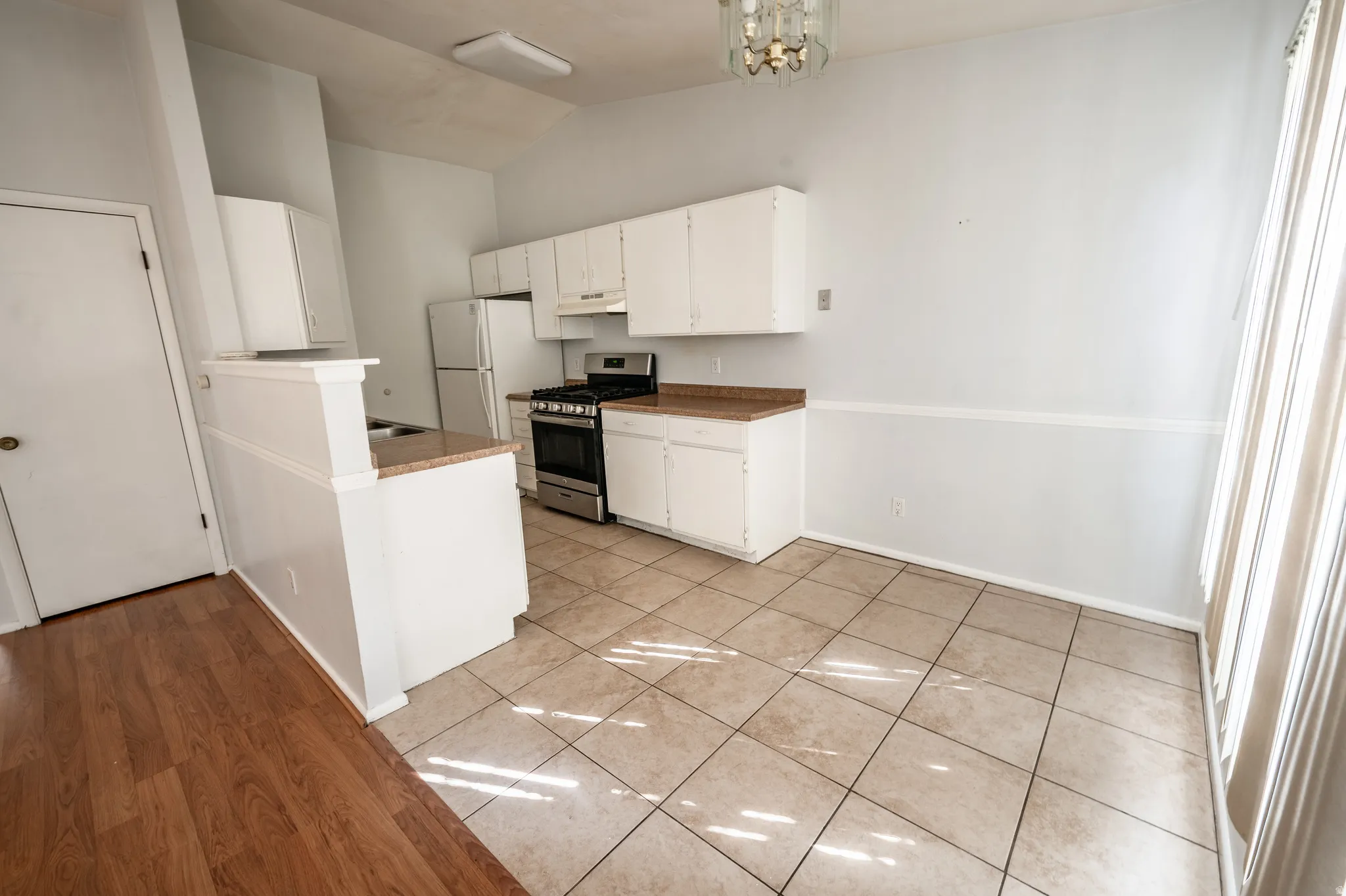 Kitchen featuring vaulted ceiling, gas range, white cabinetry, hanging lights, and light tile patterned floors