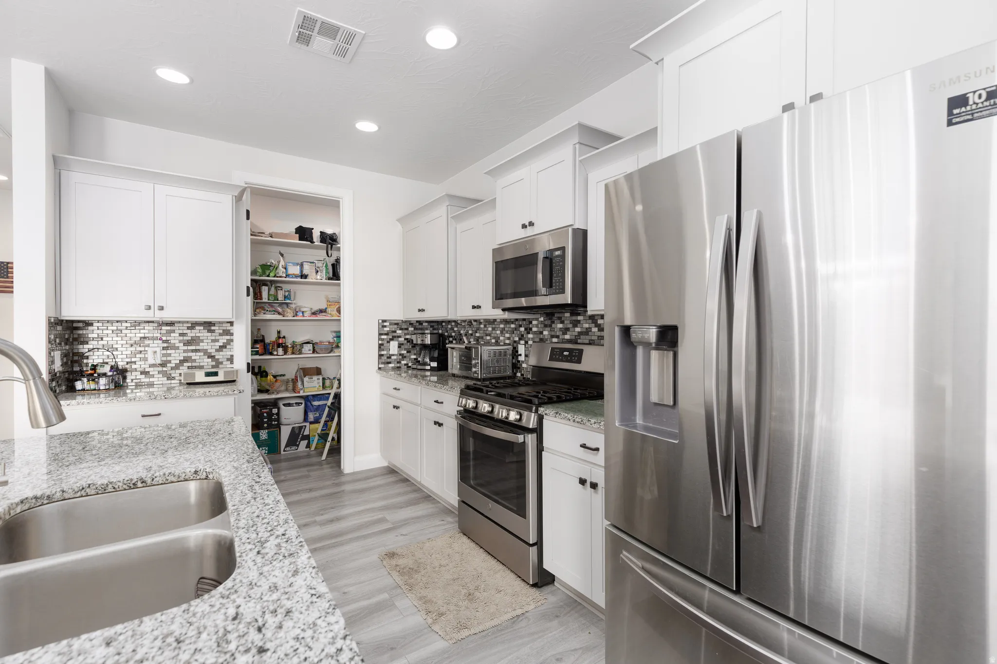 Kitchen featuring stainless steel appliances, white cabinetry, light stone countertops, recessed lighting, and backsplash
