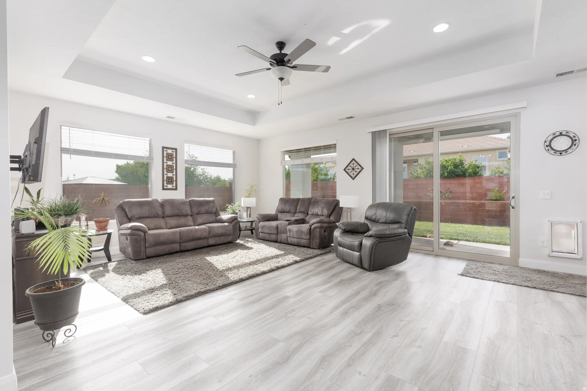 Living room featuring a ceiling fan, a tray ceiling, plenty of natural light, light wood-style flooring, and recessed lighting
