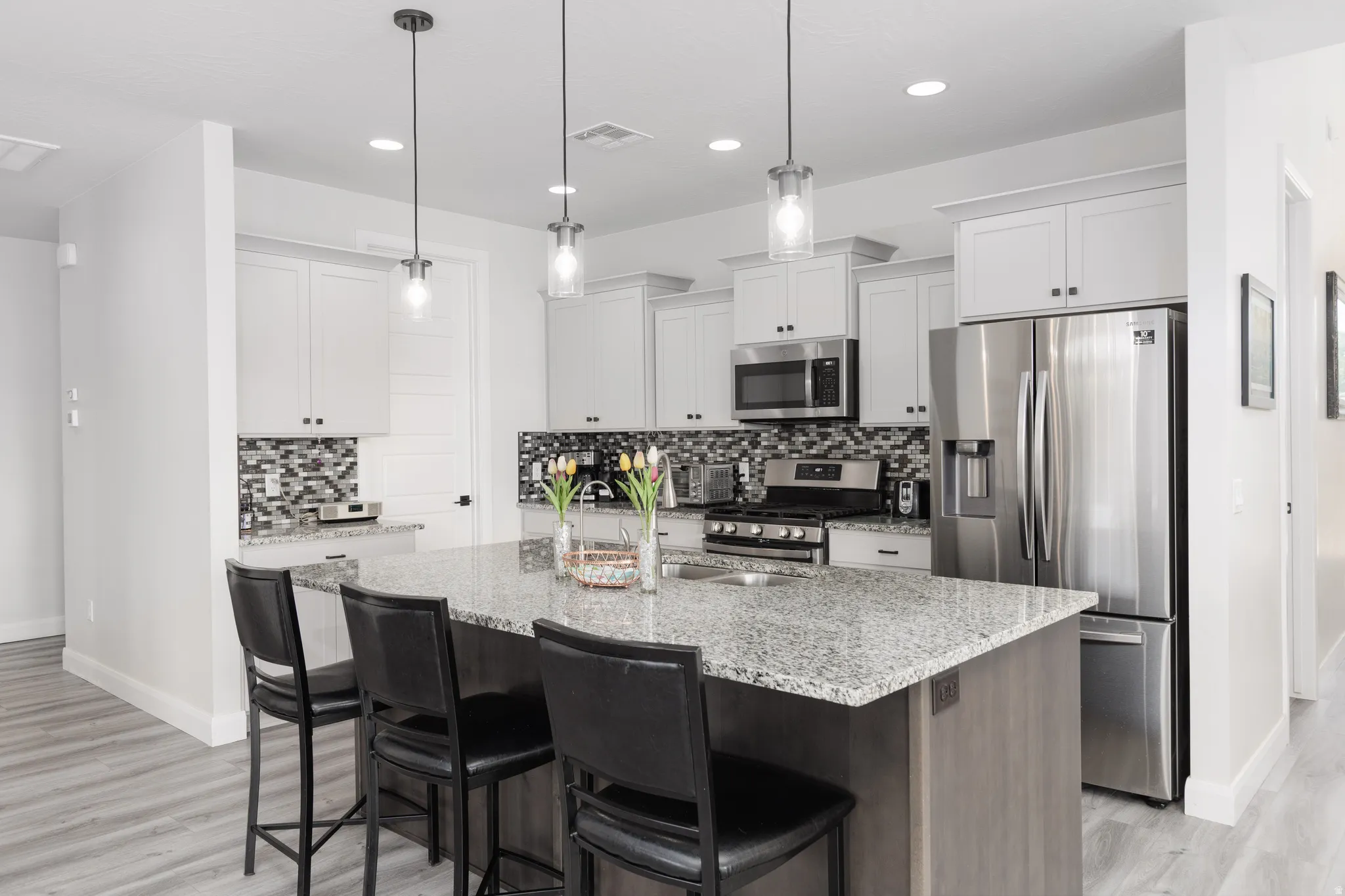 Kitchen featuring stainless steel appliances, light stone countertops, a kitchen island with sink, a kitchen bar, and tasteful backsplash