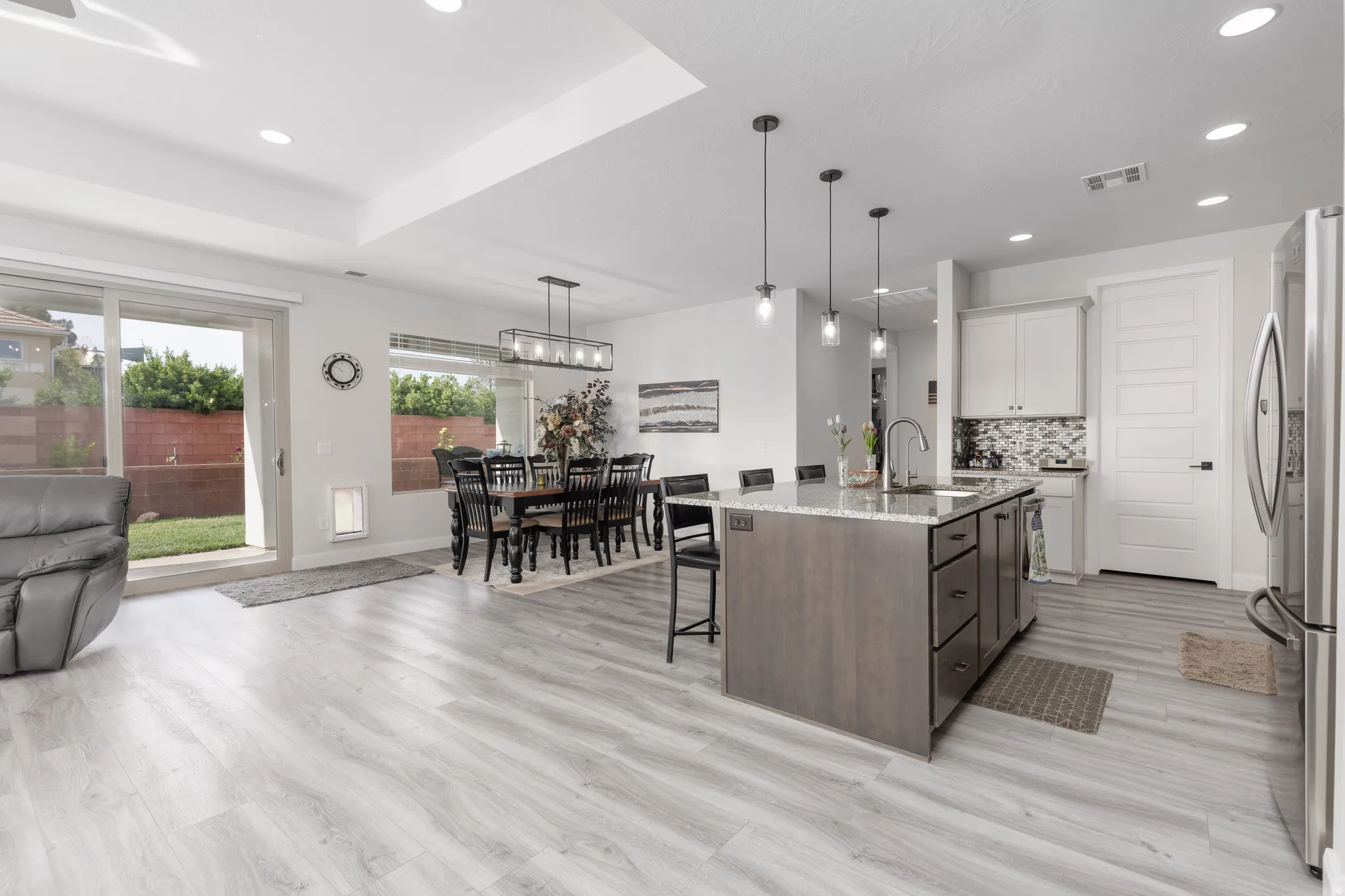 Kitchen with light stone counters, two tone cabinetry, a kitchen breakfast bar, decorative light fixtures, and an island with sink