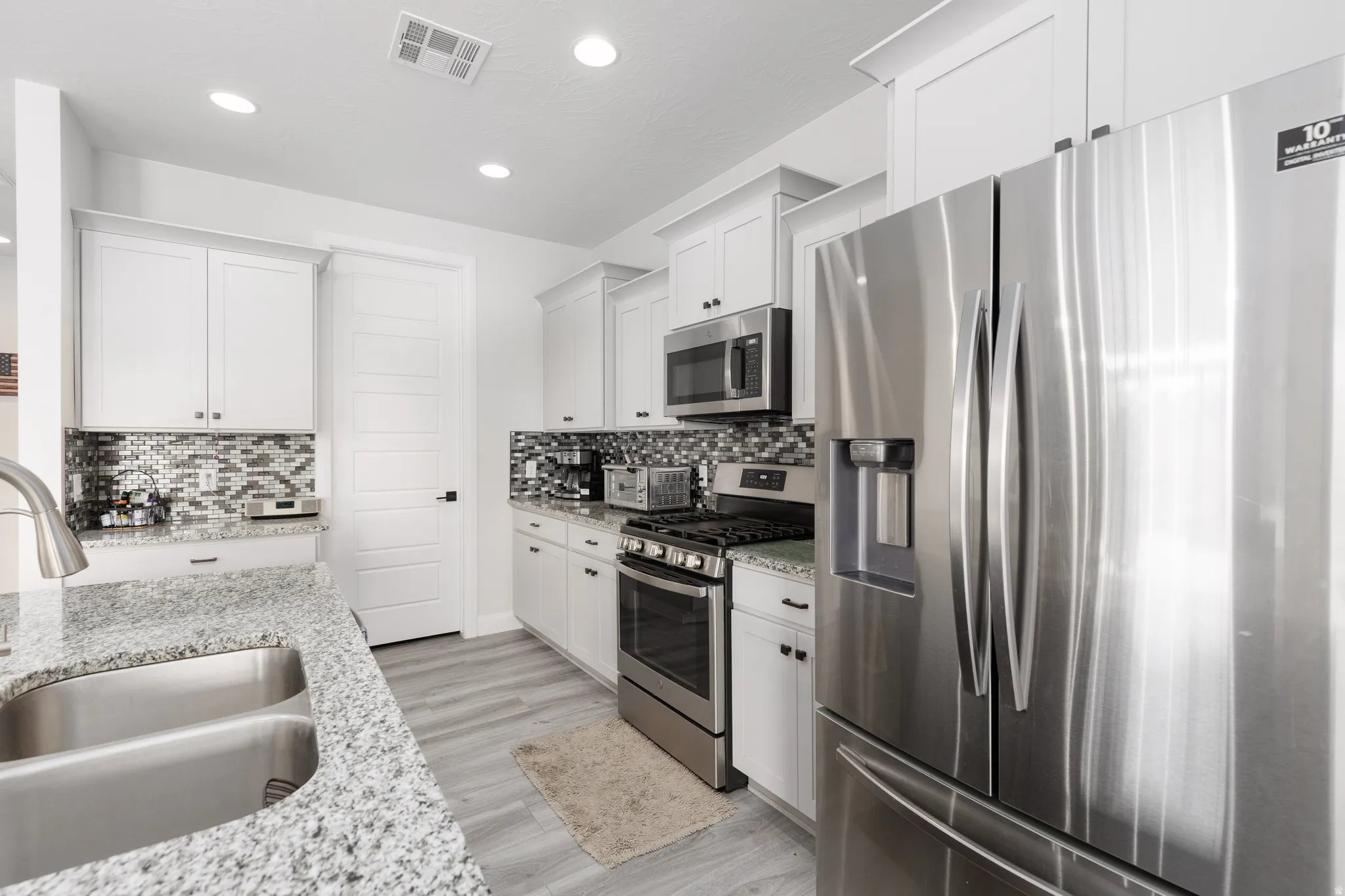 Kitchen featuring stainless steel appliances, white cabinetry, light stone counters, recessed lighting, and light wood-style floors