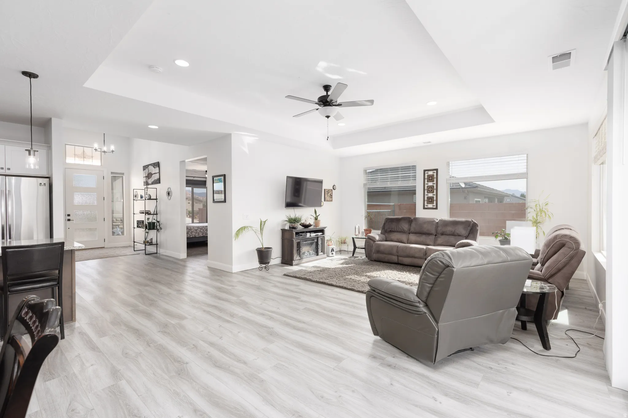 Living area featuring ceiling fan, light wood-style floors, a tray ceiling, and hanging lights