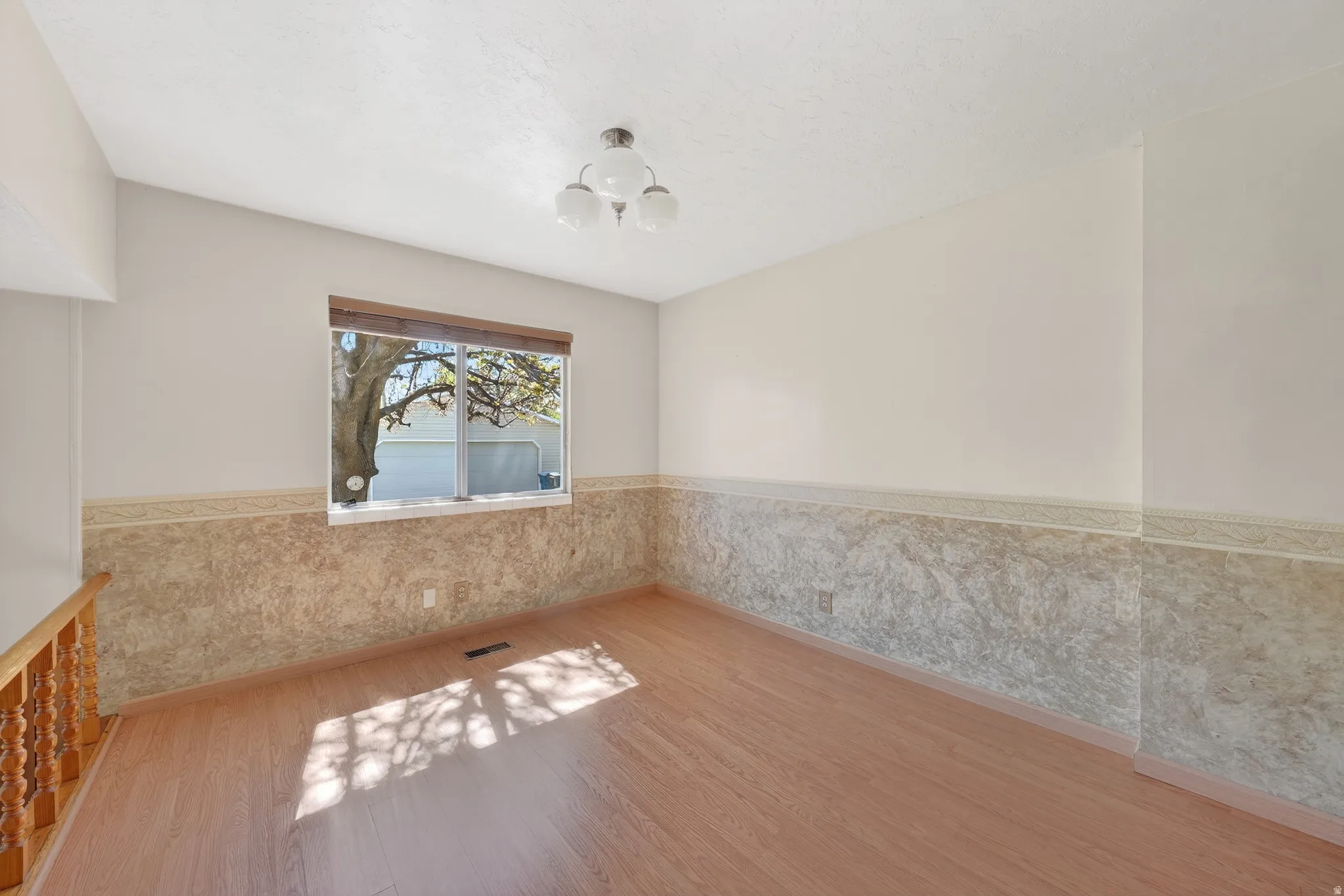 Empty room with wainscoting, light wood finished floors, and suspended lighting