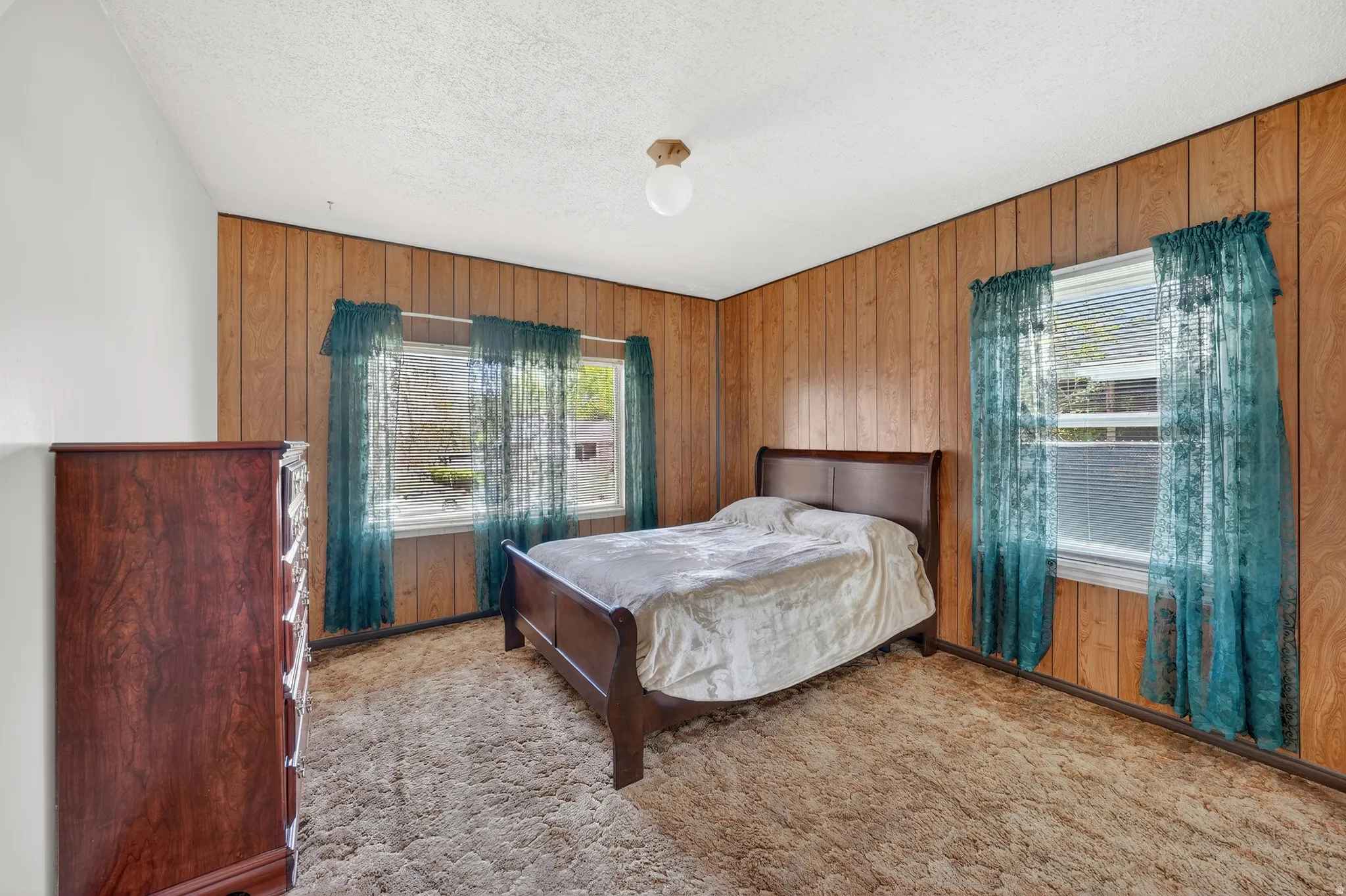 Bedroom with wooden walls, carpet flooring, and a textured ceiling