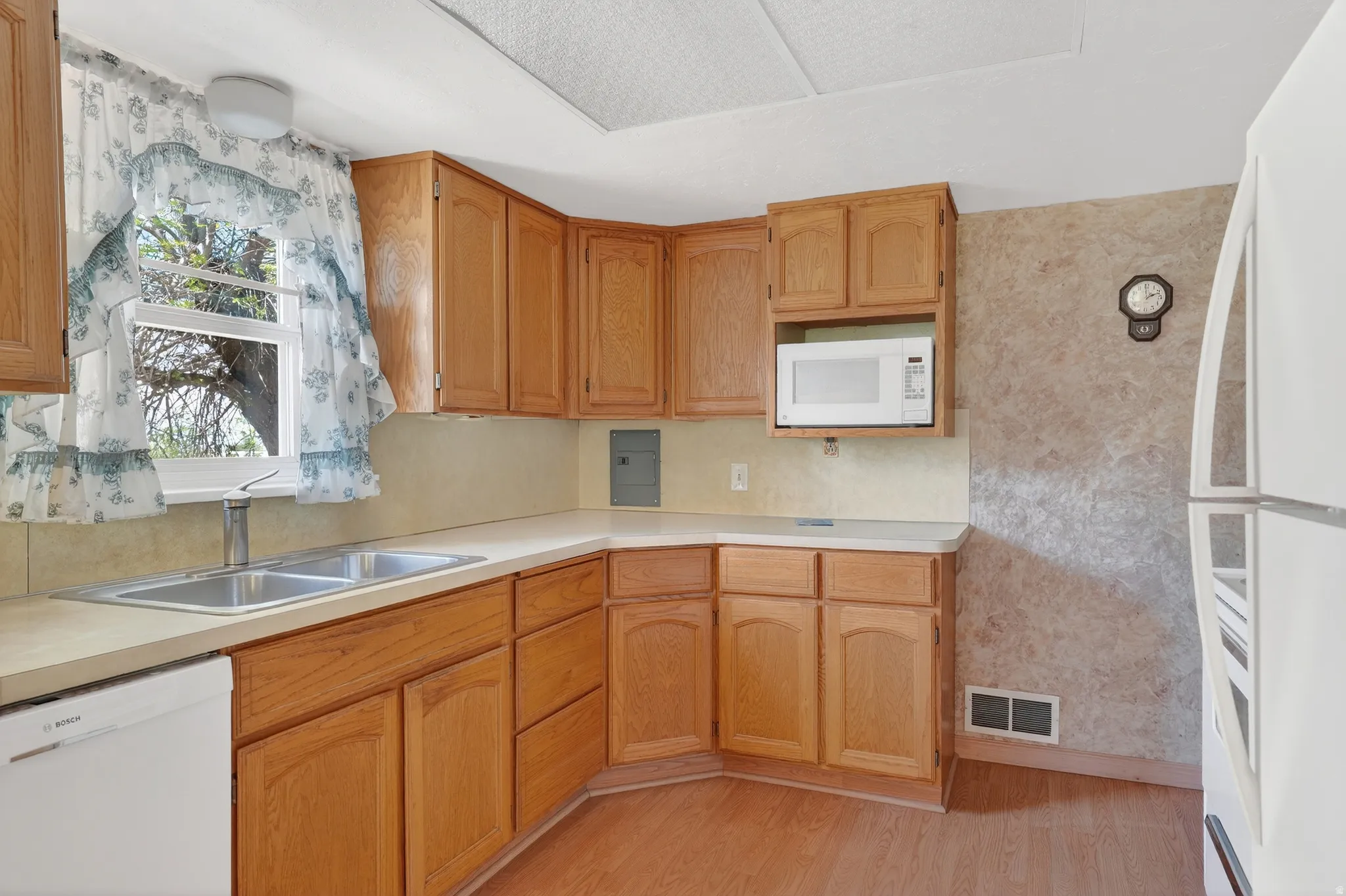 Kitchen with wallpapered walls, white appliances, light countertops, light wood-type flooring, and wood finish cabinets