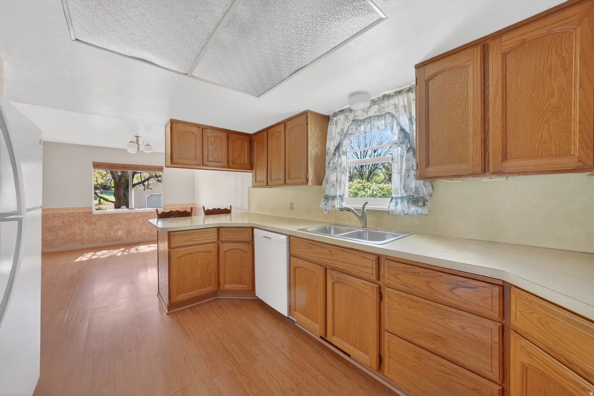 Kitchen featuring light countertops, light wood-style flooring, white appliances, and wood finish cabinetry