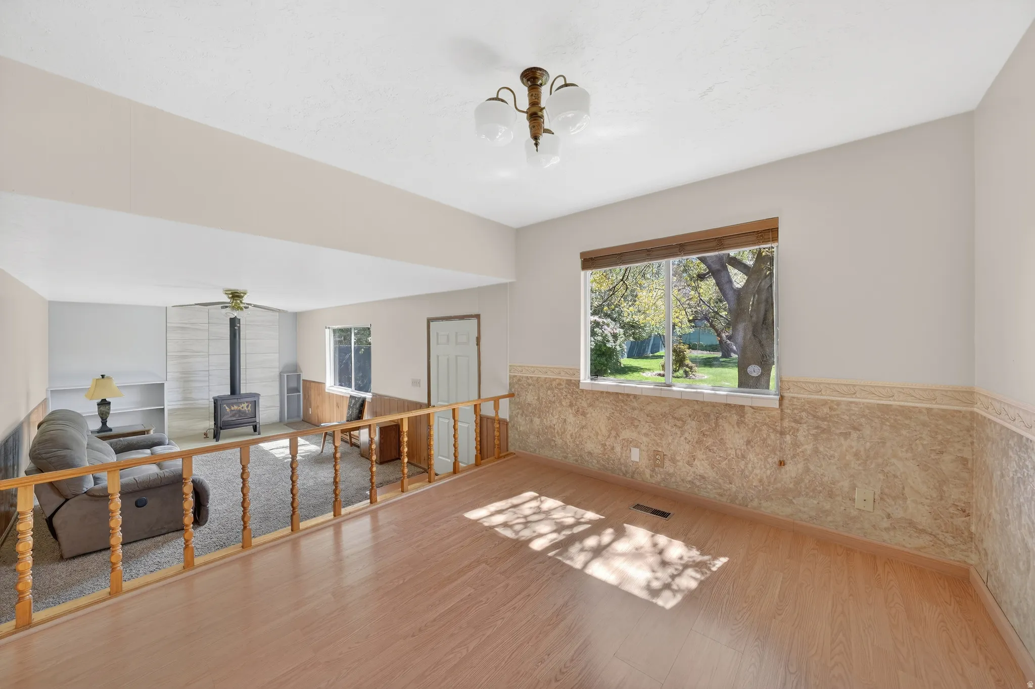 Interior space with a wainscoted wall, wood finished floors, a wood stove, and ceiling fan