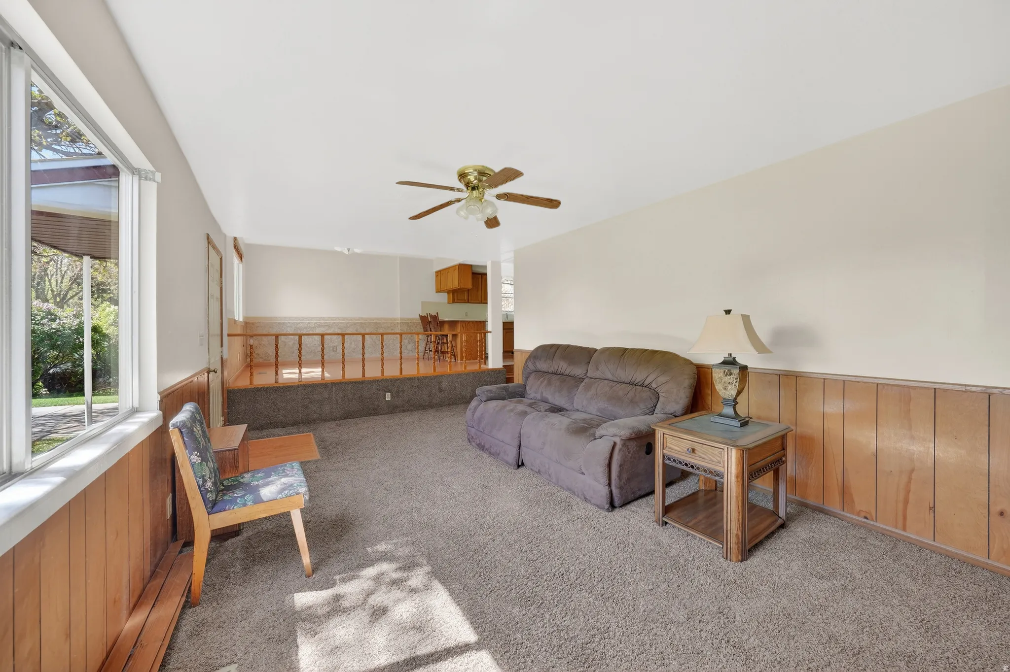 Living area featuring wood walls, a wainscoted wall, light carpet, healthy amount of natural light, and a ceiling fan