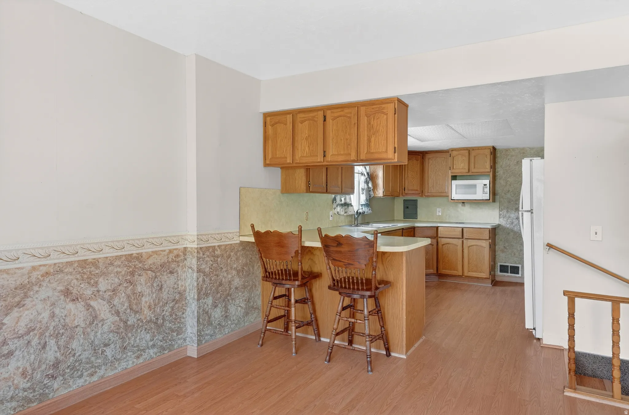 Kitchen featuring light countertops, a peninsula, wood finish cabinetry, a kitchen breakfast bar, and light wood-style flooring