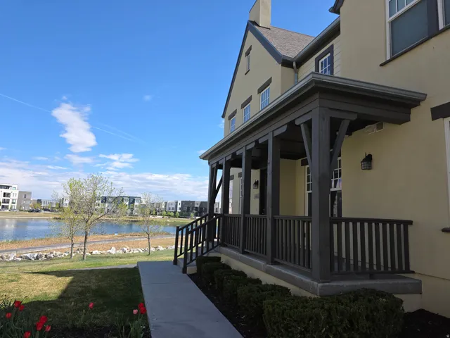View of side of property featuring a lawn, a porch, stucco siding, a water view, and a chimney