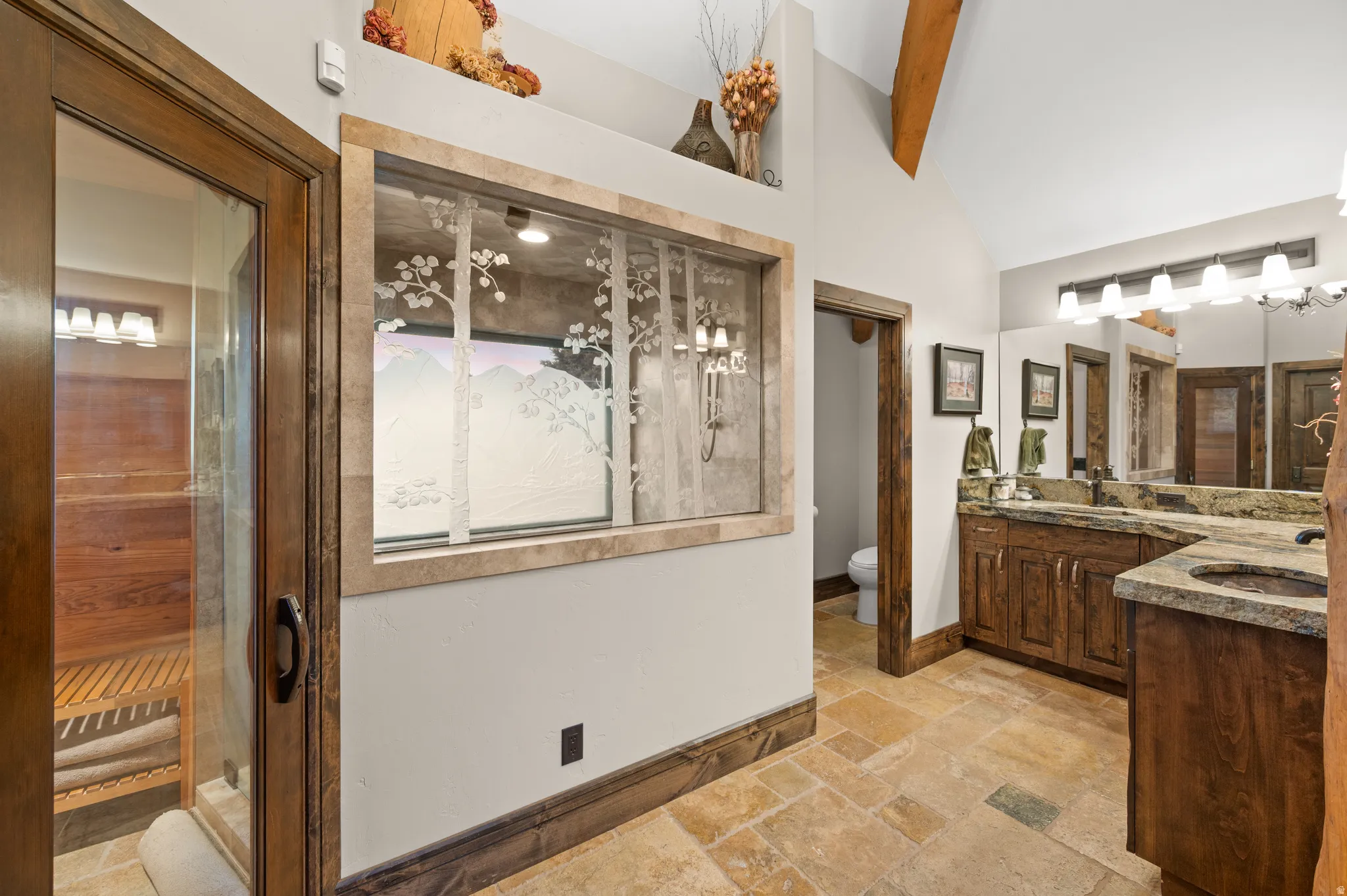 Bathroom featuring double vanity, stone tile floors, a relaxing sauna, vaulted ceiling, and a stall shower