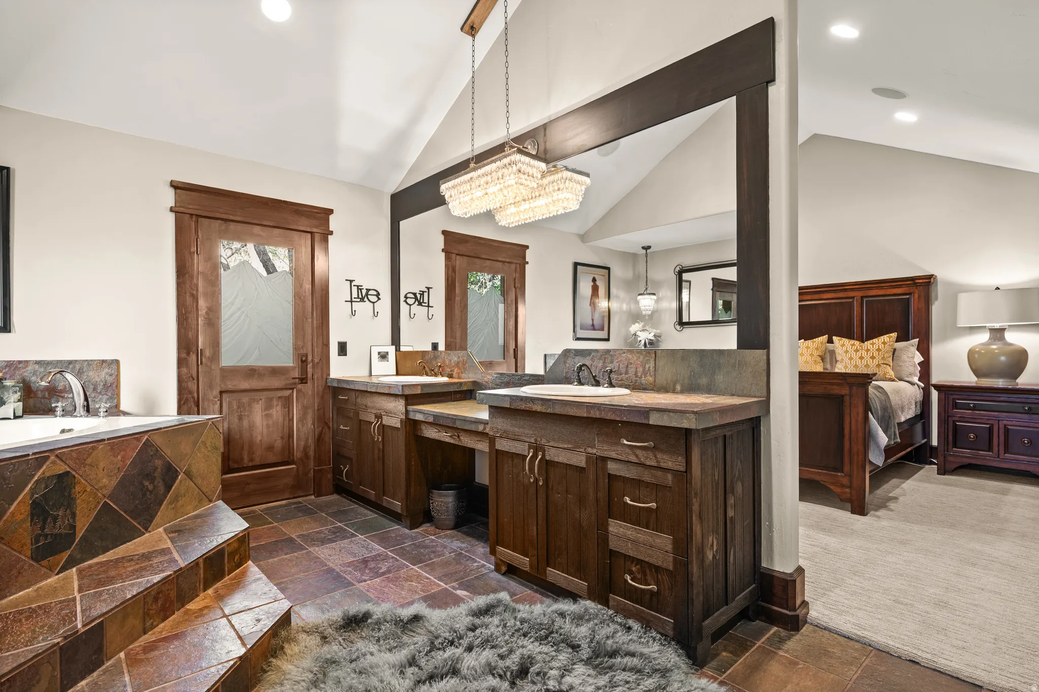 Ensuite primary bedroom bathroom with recessed lighting, double vanity, stone tile floors, a garden tub, and lofted ceiling