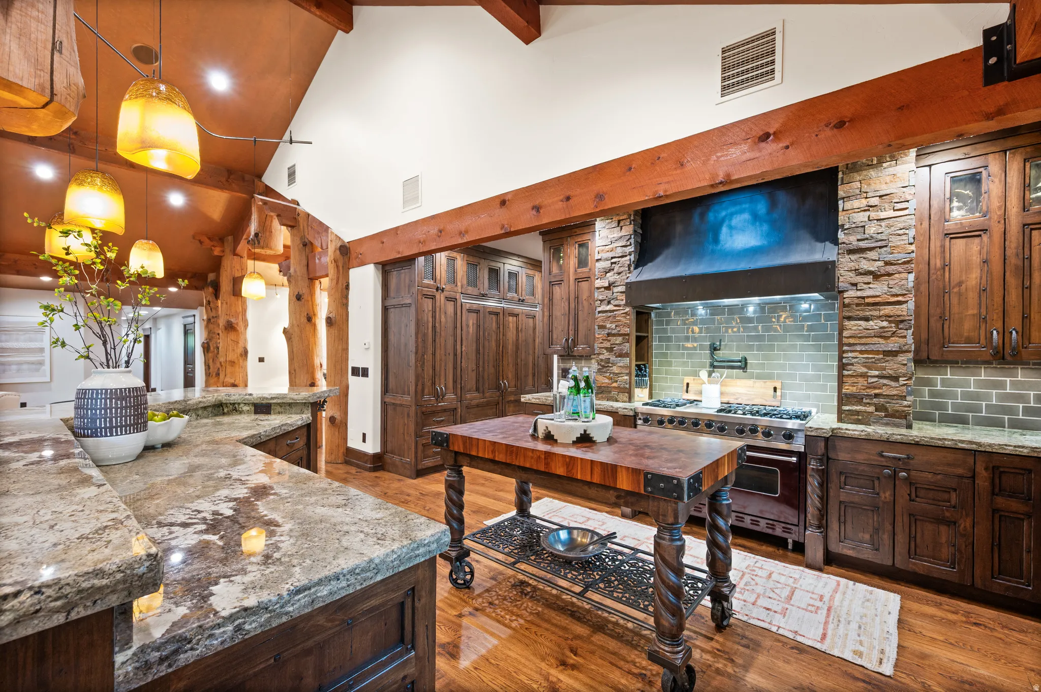 Kitchen with light stone countertops, dark wood finish cabinets, range hood, hanging light fixtures, and double oven range